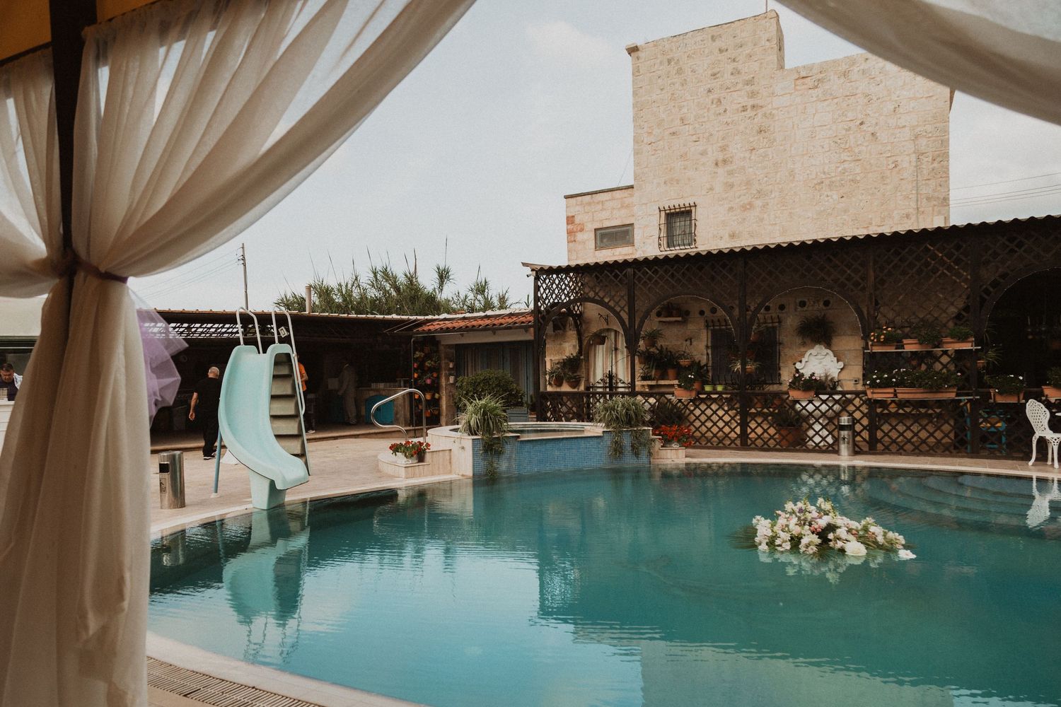 Elegant poolside wedding venue with white drapes and Mediterranean-style architecture.