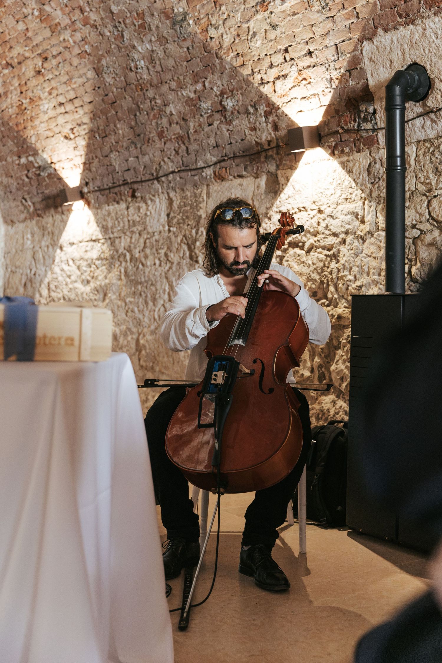 Musician plays cello during wedding ceremony in atmospheric brick venue.