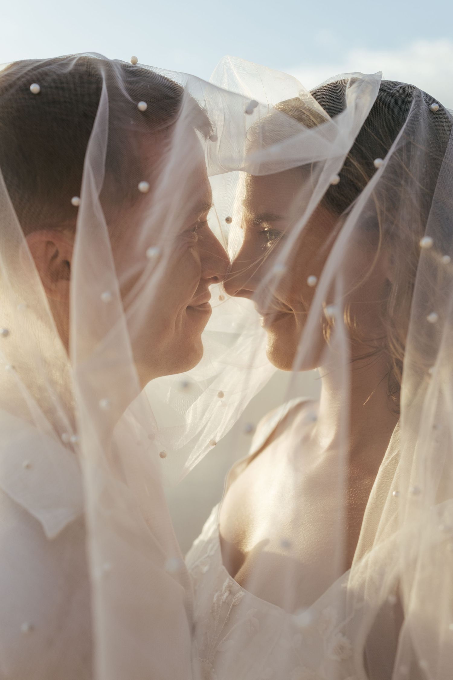 Multiple brides wearing white veils stand together in soft sunlight creating an ethereal artistic composition. Praia do Castelejo, Portugal.