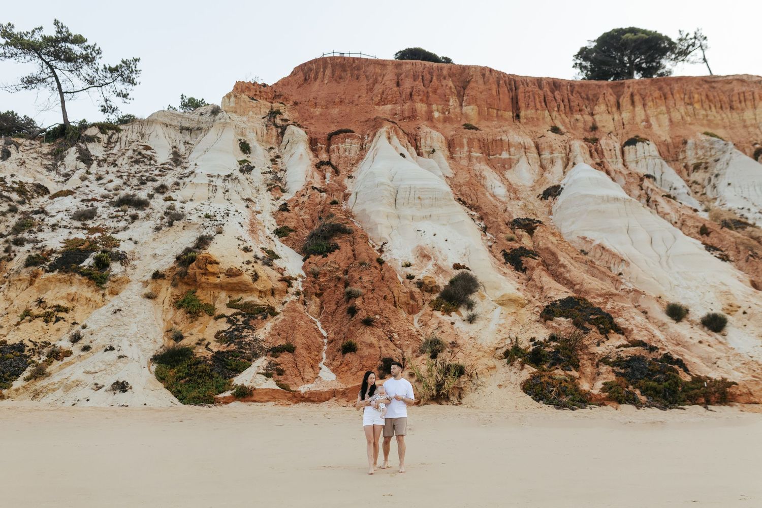Two figures stand at the base of colorful sandstone cliffs along a beach at sunset in Brazil.