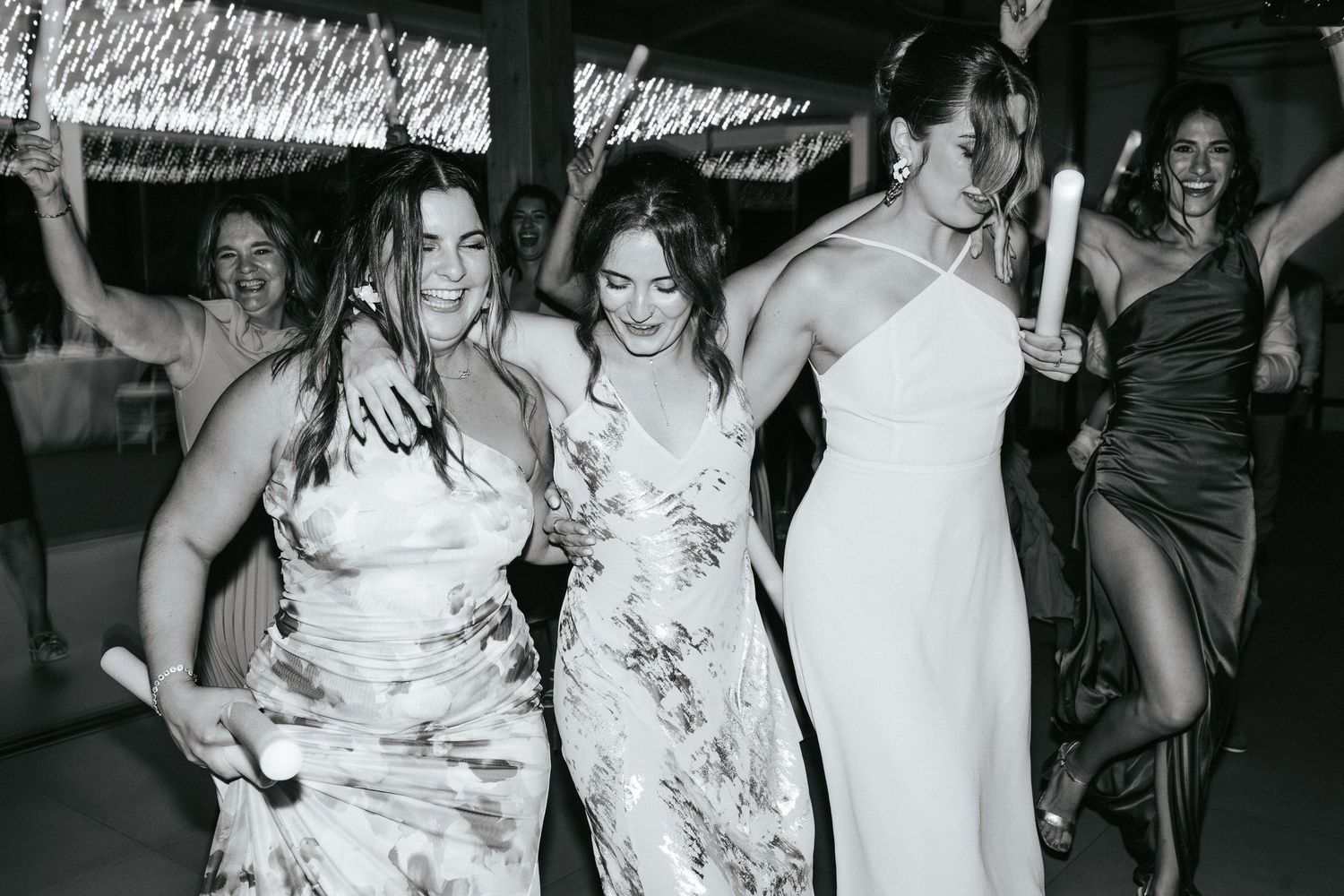 Women in formal dresses dancing and laughing at a wedding reception.