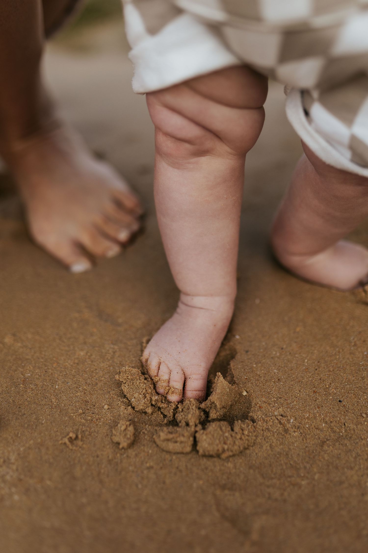 Close up of a baby's chubby feet and toes squishing into brown sand or dirt on the ground.