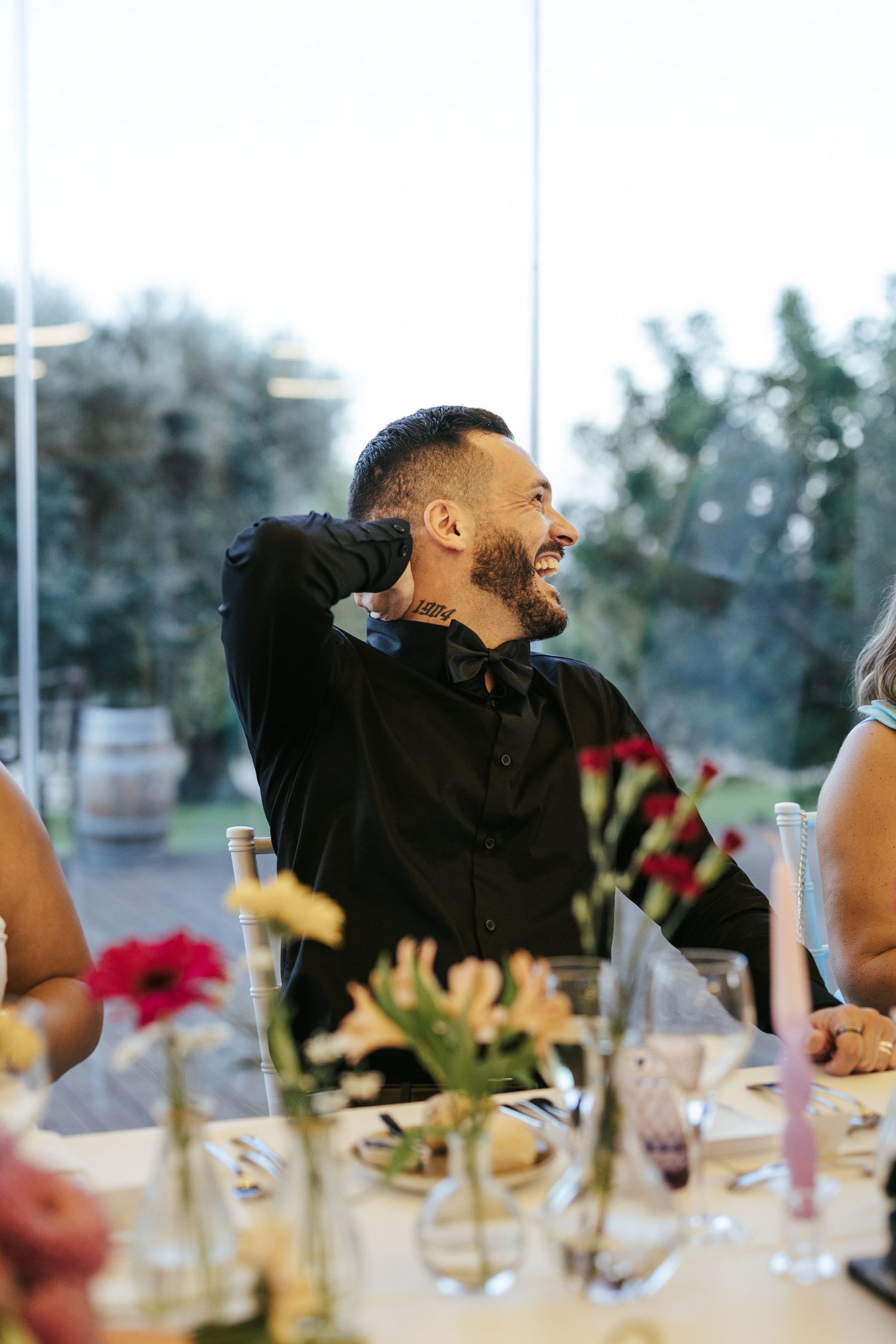 Person laughing joyfully at an elegant dining table set with flowers and glassware.