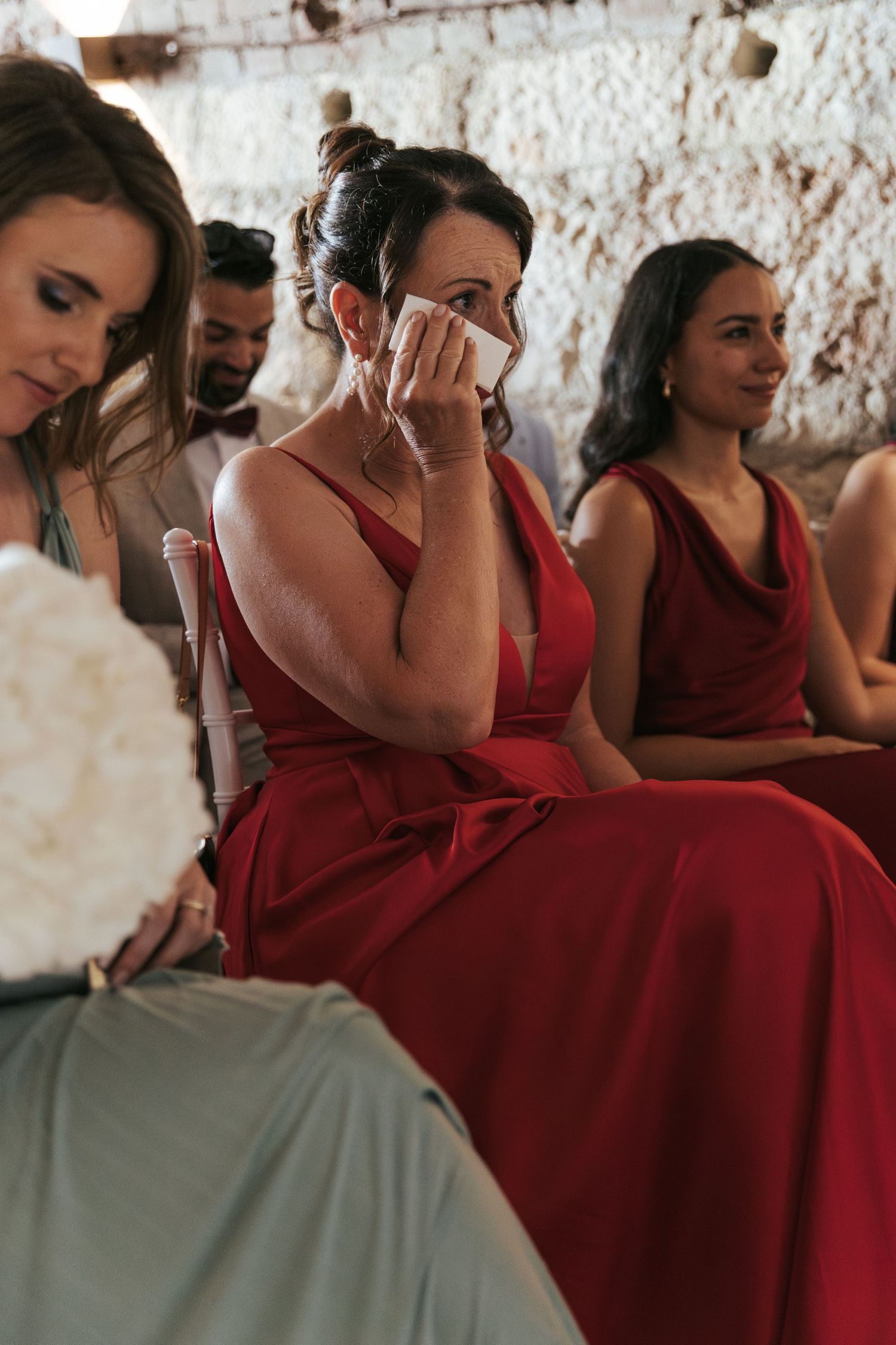 Bridesmaids in deep red dresses seated together during an emotional wedding moment.