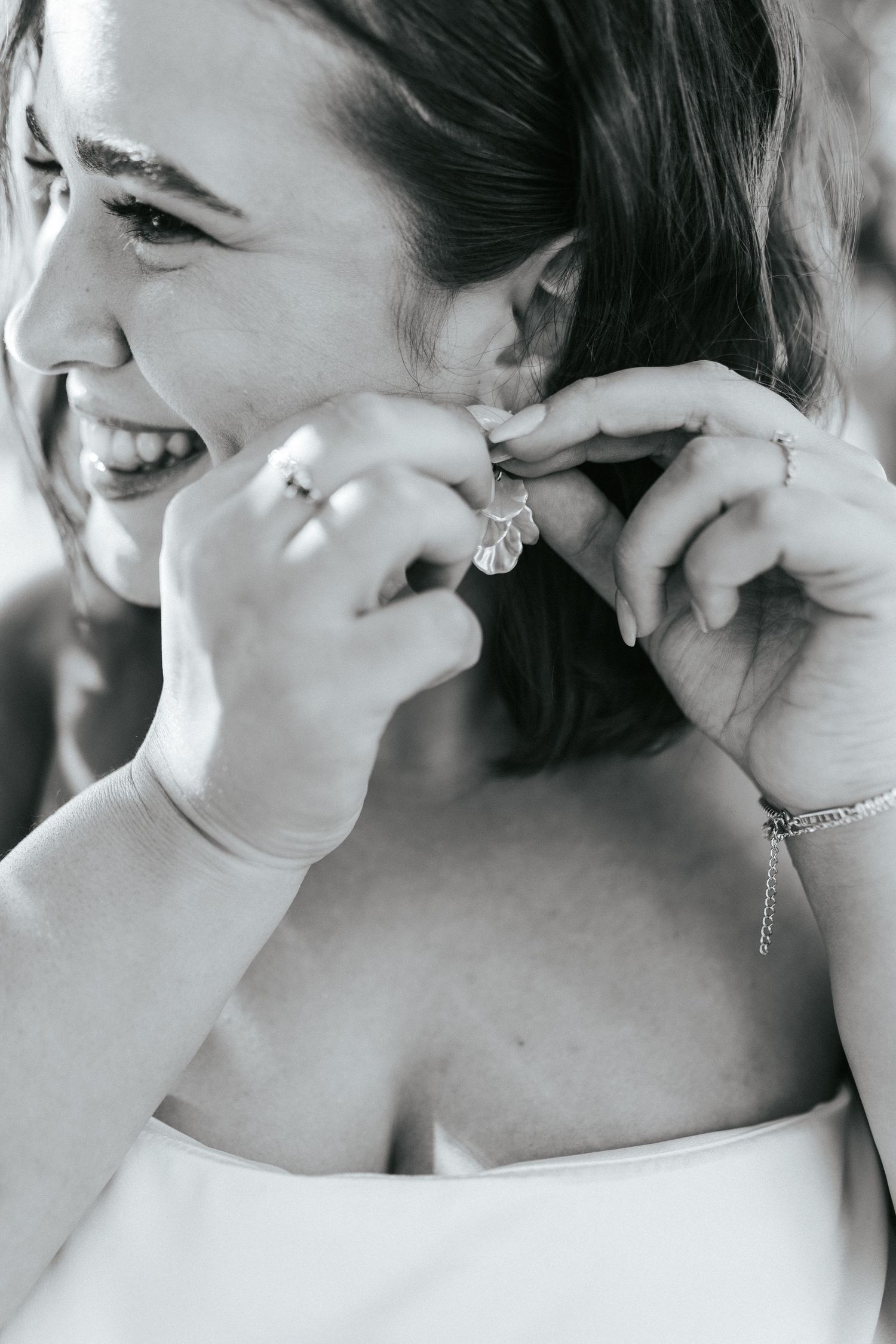 Close-up of someone putting on an earring in a white dress with joyful expression.