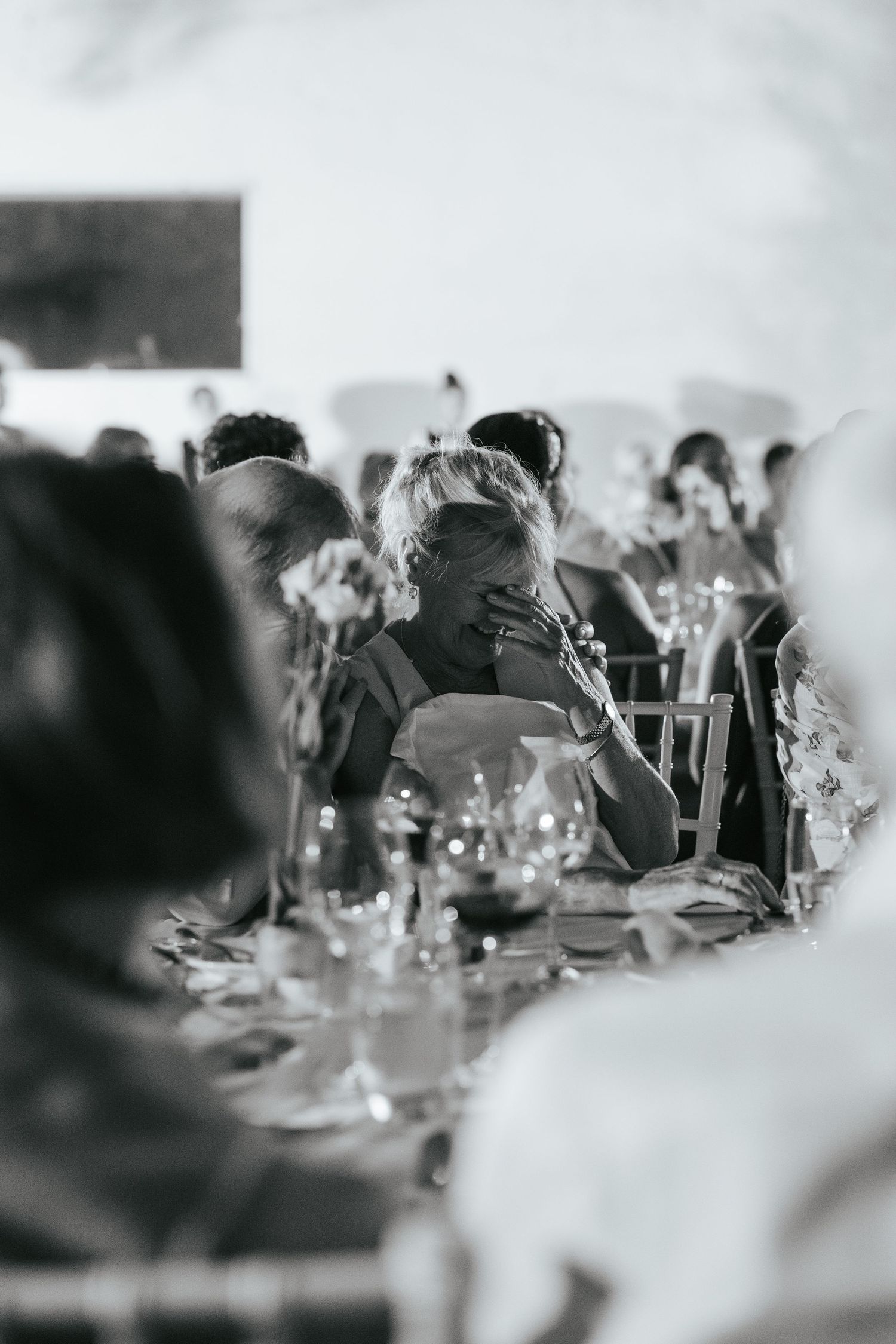 Emotional wedding guest wiping tears at reception table in candid black and white wedding photography.