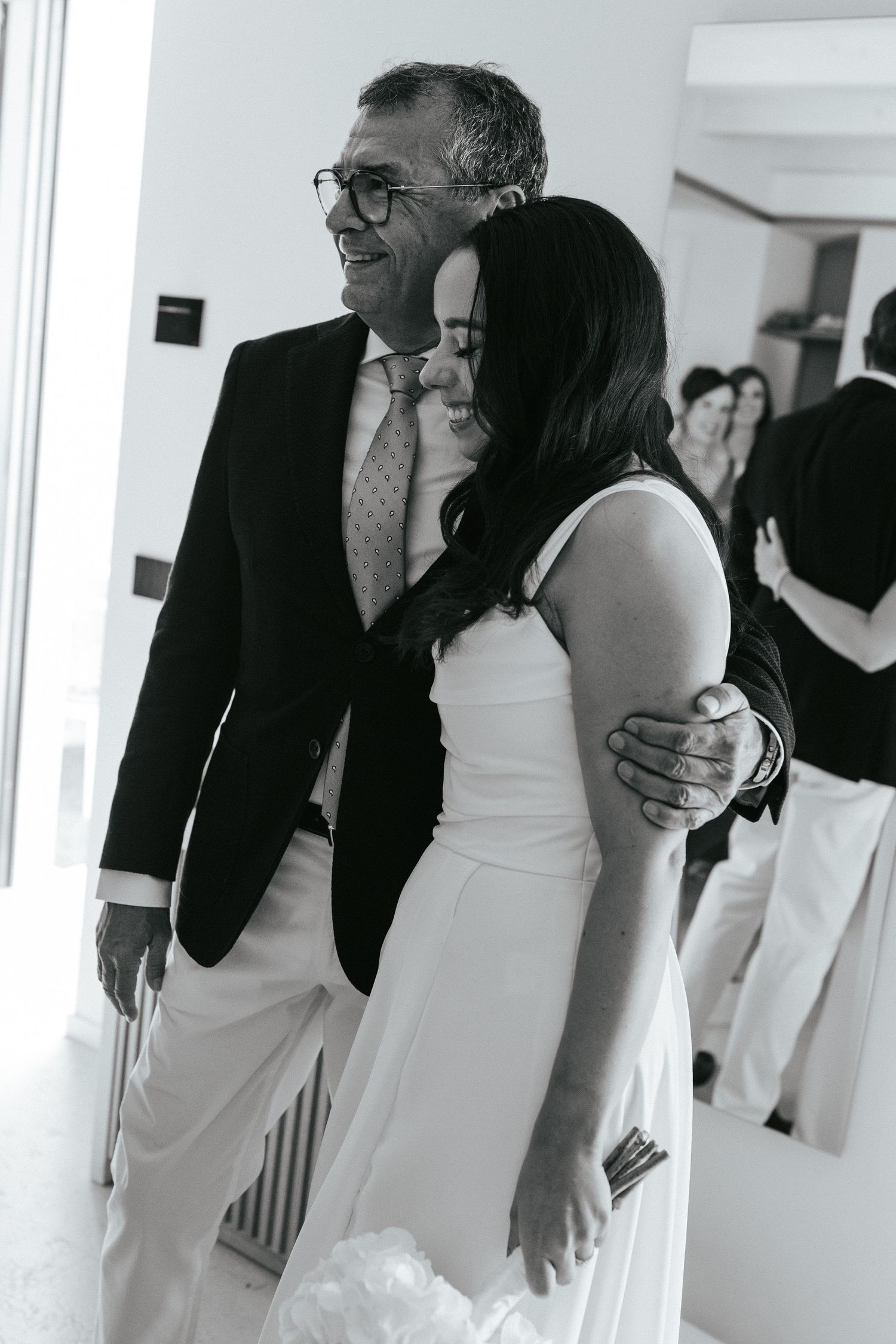 Black and white photo of wedding guests sharing joyful moments in formal attire.