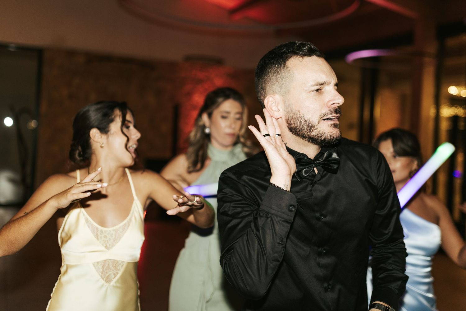 People dancing and enjoying themselves at a dark reception venue with colorful lighting effects.