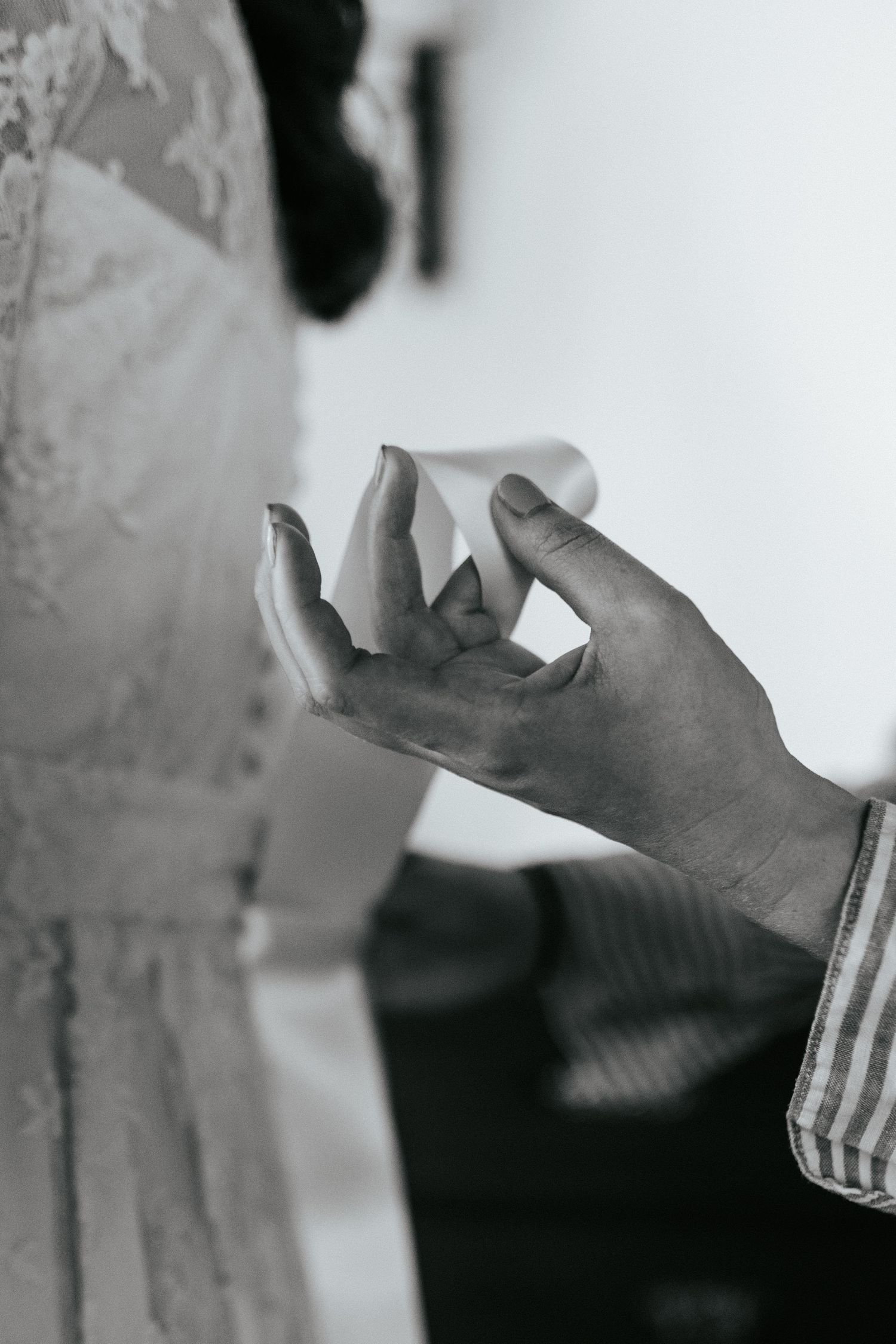 Black and white close-up of hands showing a delicate moment during a wedding ceremony preparation.