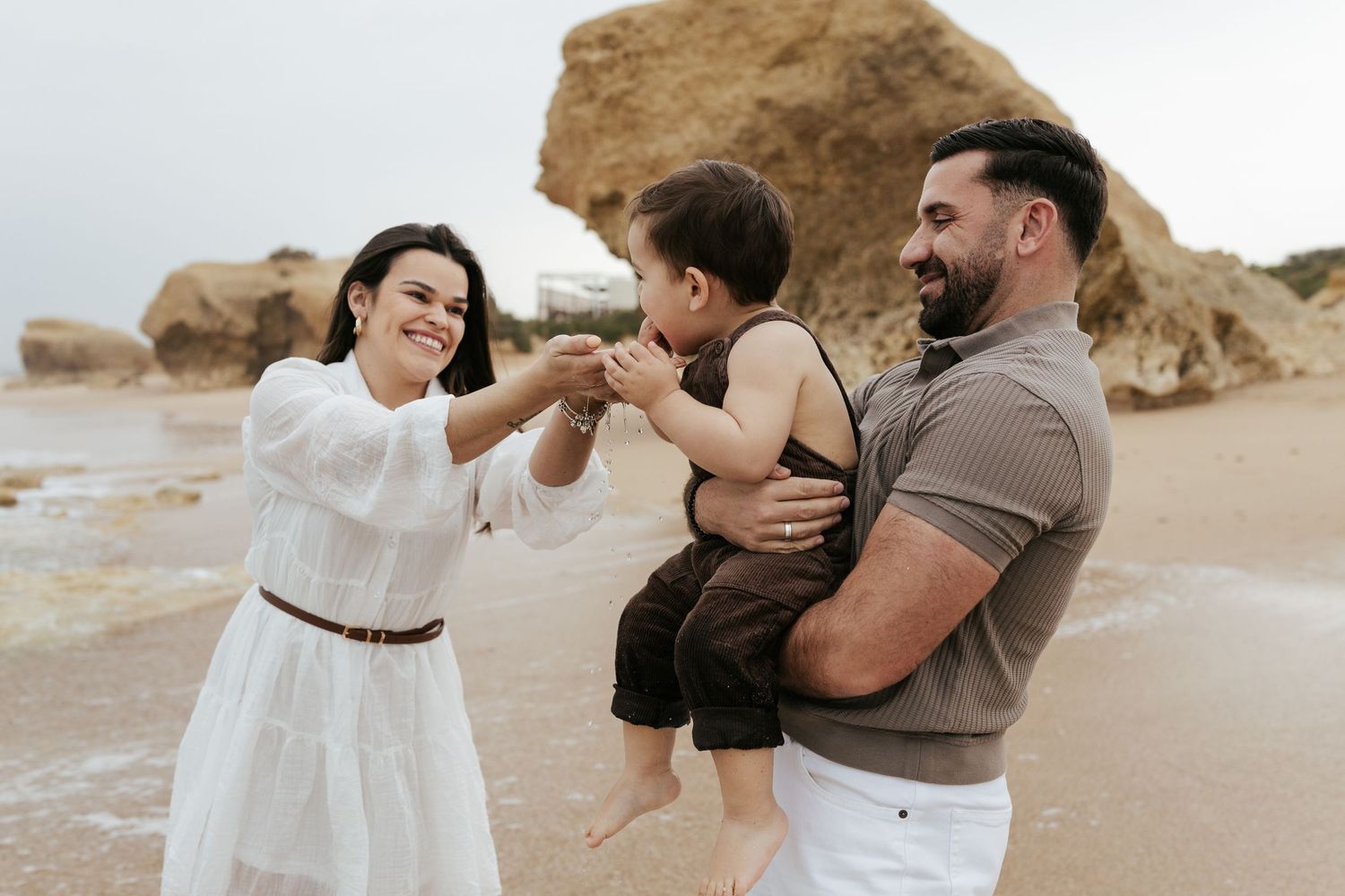A family shares a joyful moment together on a beach with rocky formations in the background.