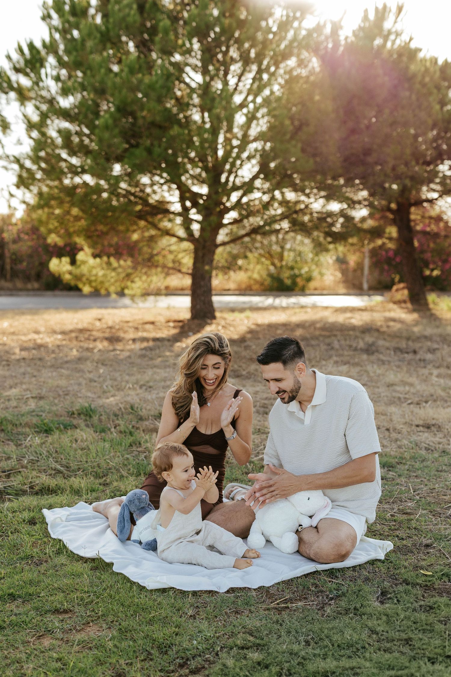 Family enjoying a picnic together on a white blanket in a grassy park during golden hour at sunset.