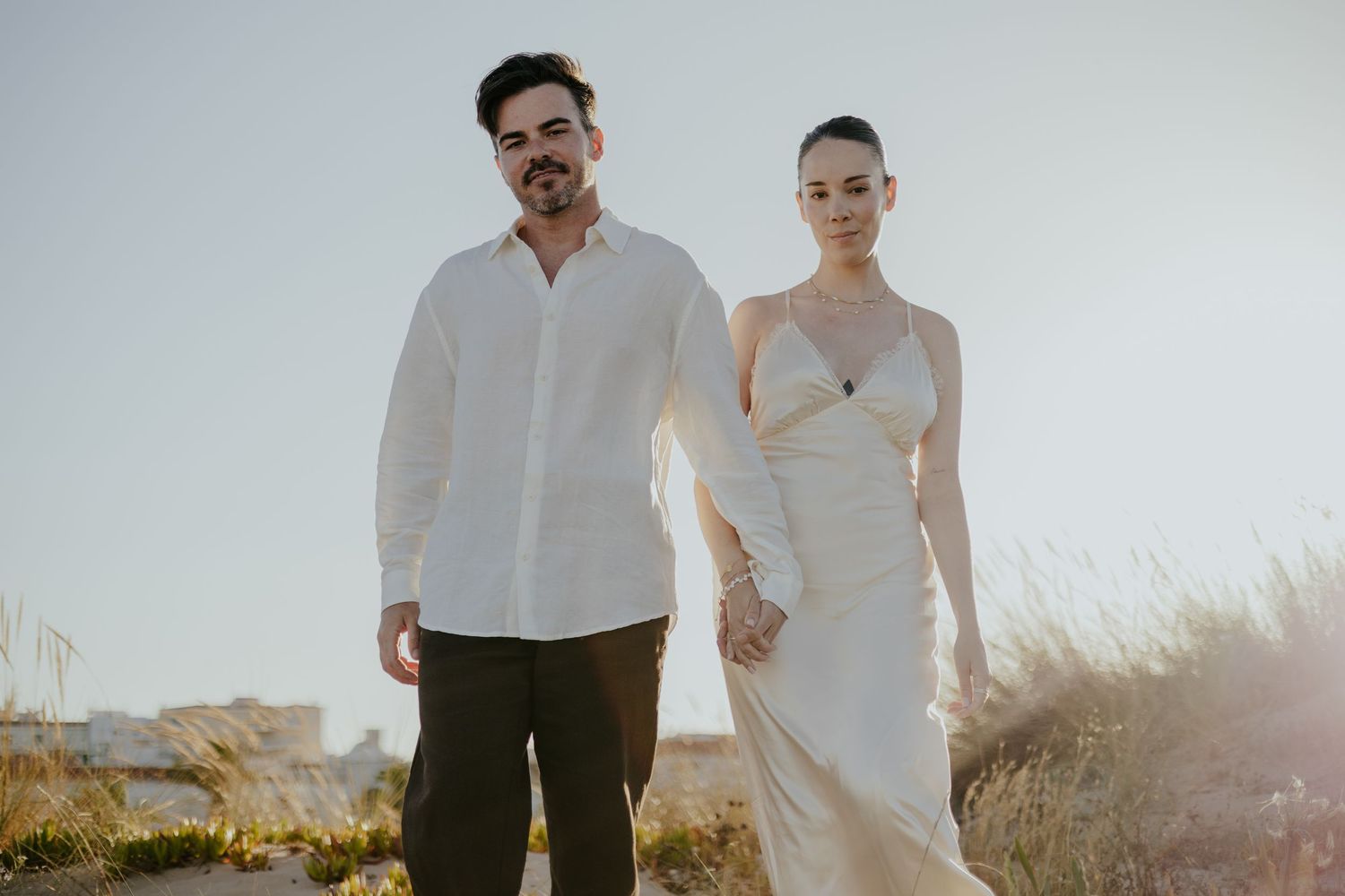 Elegant couple in white formal attire standing together in natural coastal setting. Meia Praia, Lagos, Algarve, Portugal.