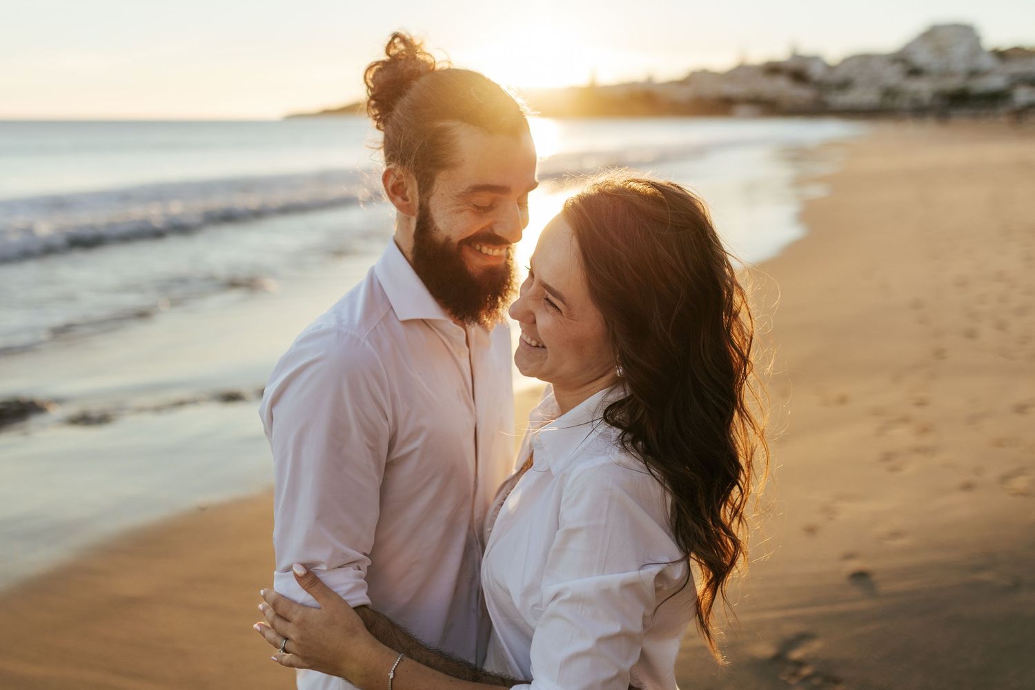 A romantic couple embraces during golden hour sunset on a scenic beach. Praia da Luz, Lagos, Algarve, Portugal.
