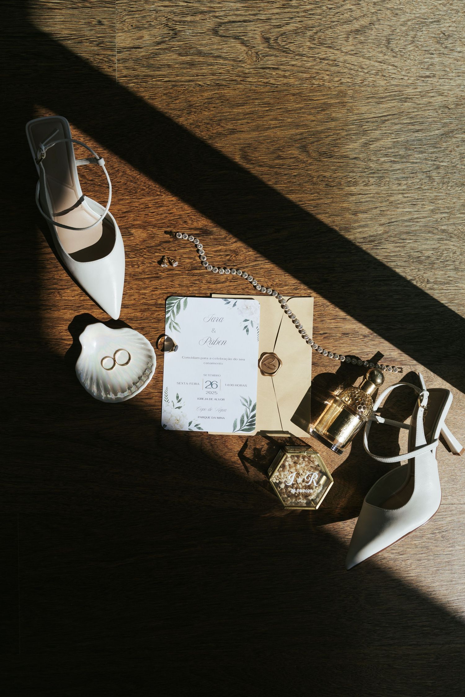 Wedding accessories including white heels, invitation cards, and decorative items arranged on a wooden surface in dramatic lighting.