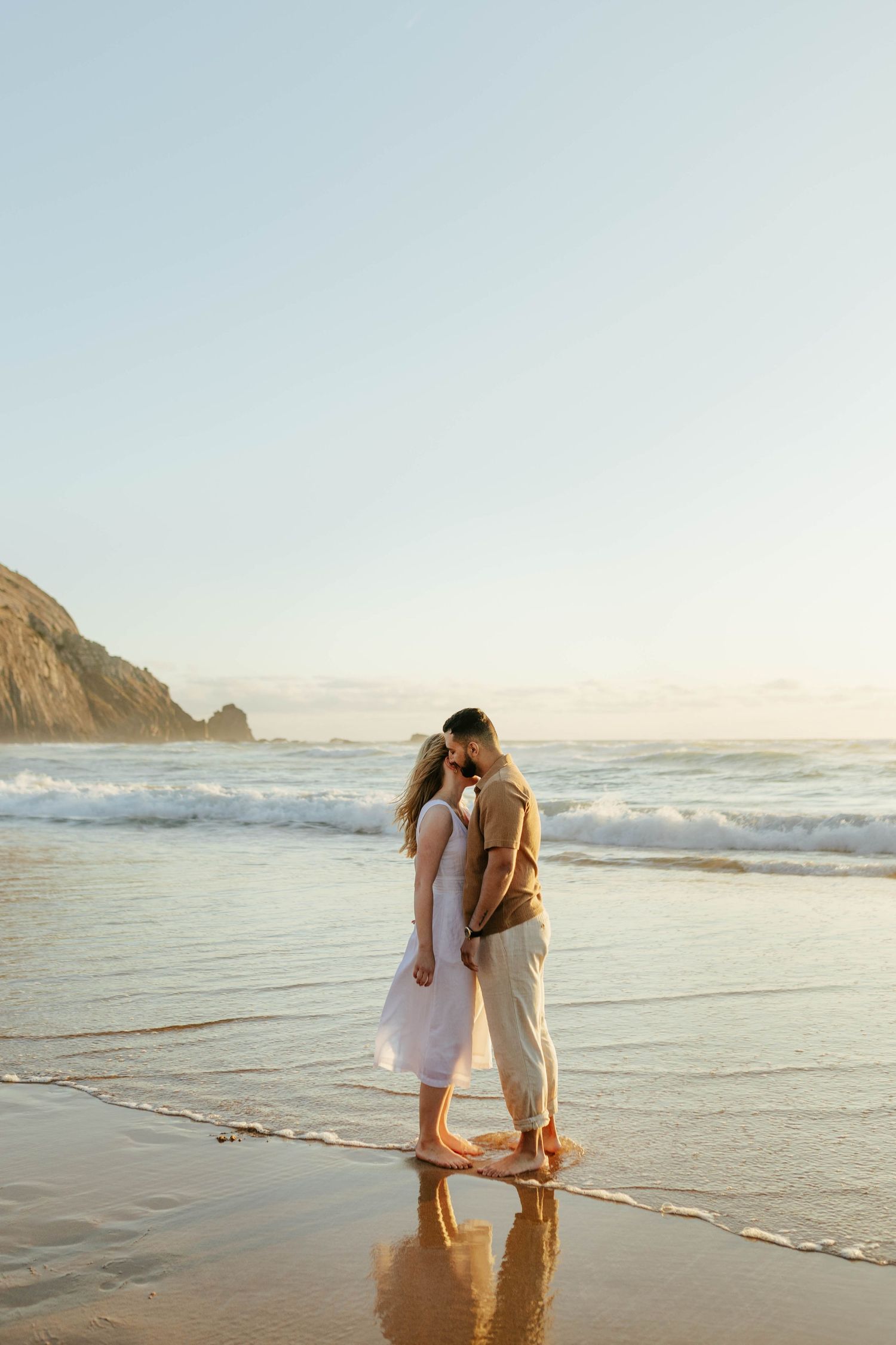 Couple sharing an intimate moment at sunset on a beach with cliffs in the background. Praia do Castelejo, Vila do Bispo, Algarve, Portugal.