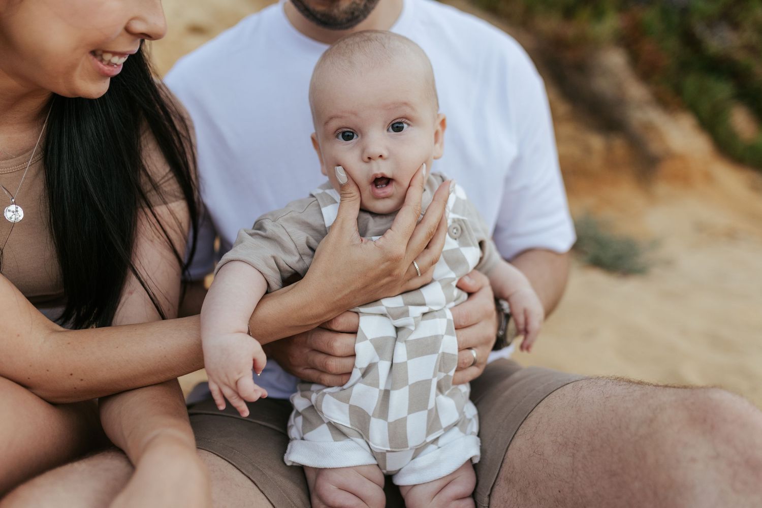 Baby in a patterned romper shows a surprised expression while being held outdoors.