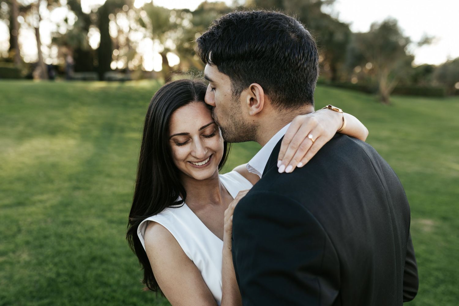 Couple sharing an intimate moment together in a green park during golden hour.