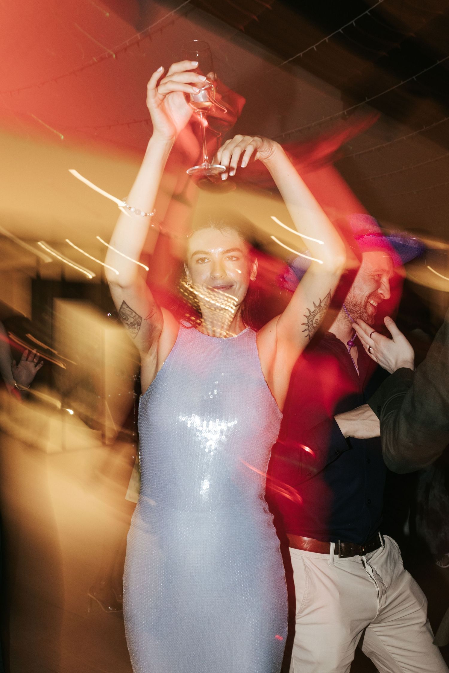 A person in a light blue sparkly dress dances energetically under red and gold lighting at a party.