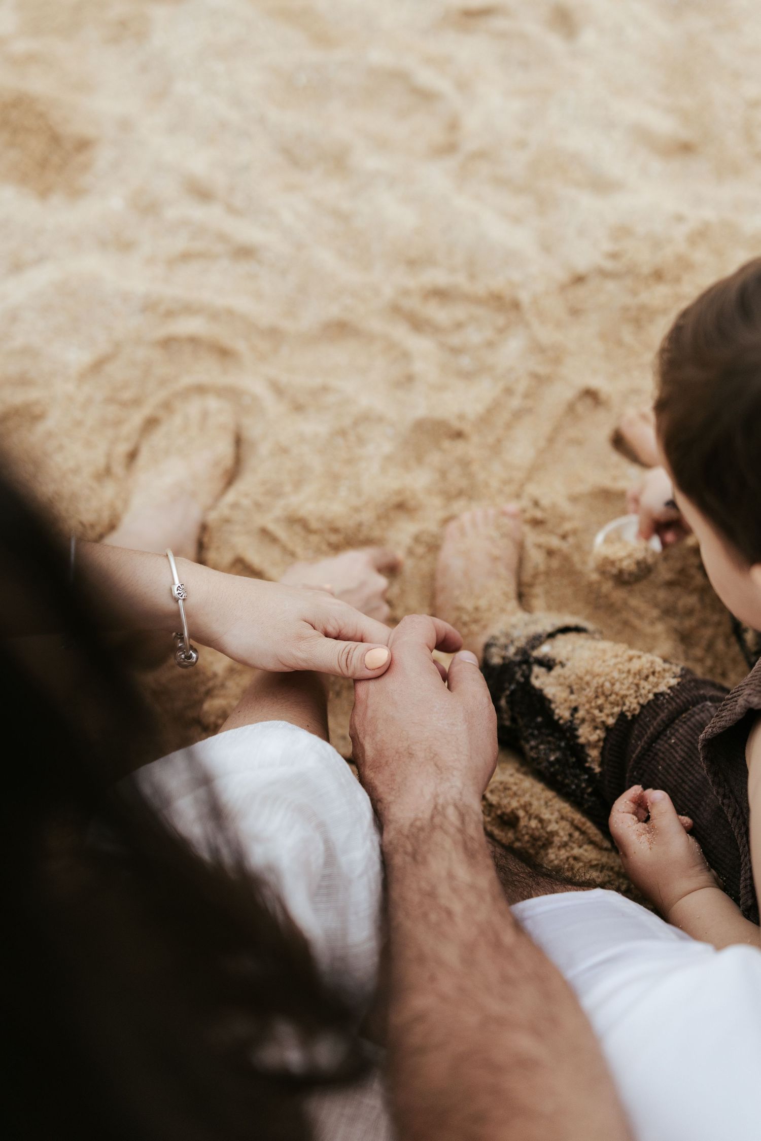 Hands playing together in soft sand on a sunny beach, with one hand wearing a delicate bracelet.