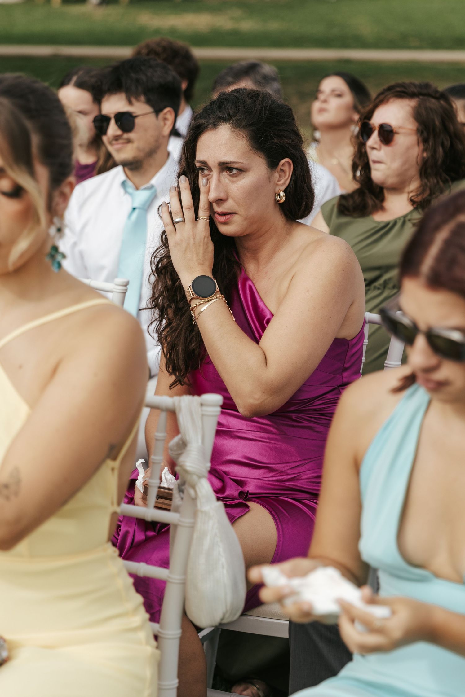 Wedding guests in colorful dresses watching ceremony outdoors with emotional reactions.