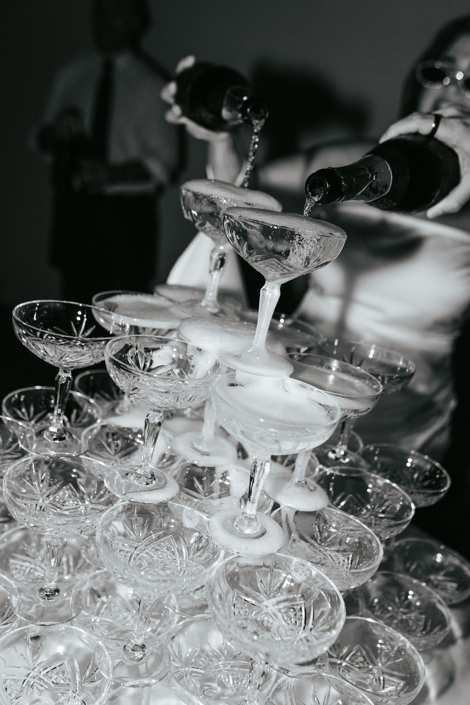 A champagne tower being filled with sparkling wine at an elegant celebration, captured in black and white.