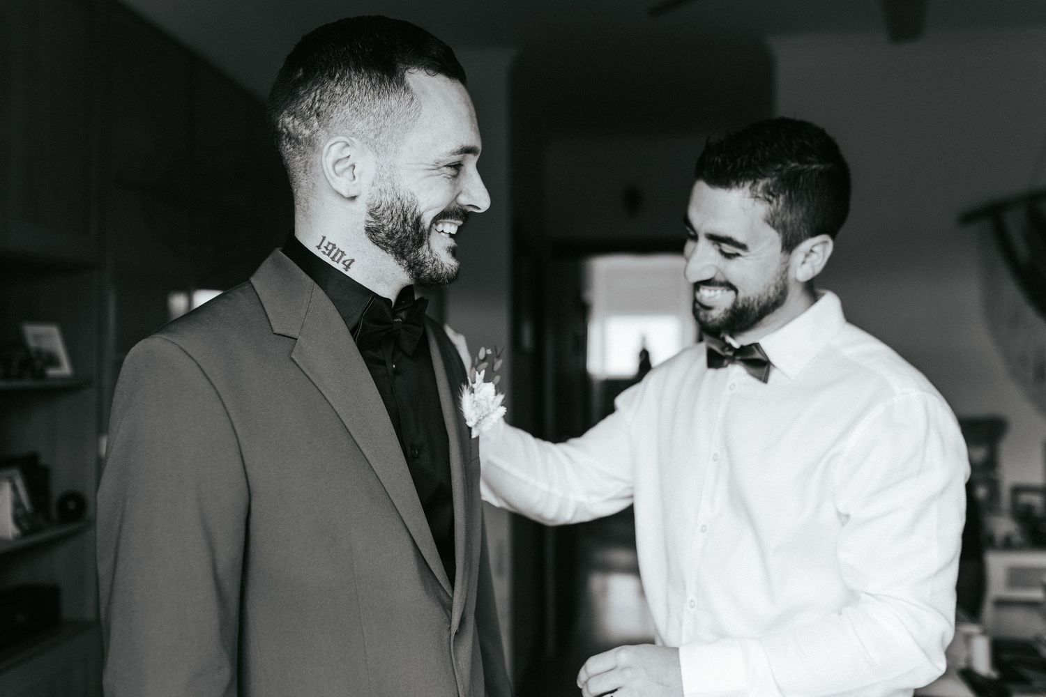 Two people sharing a joyful candid moment in black and white, with one wearing a suit and one in white formal attire.