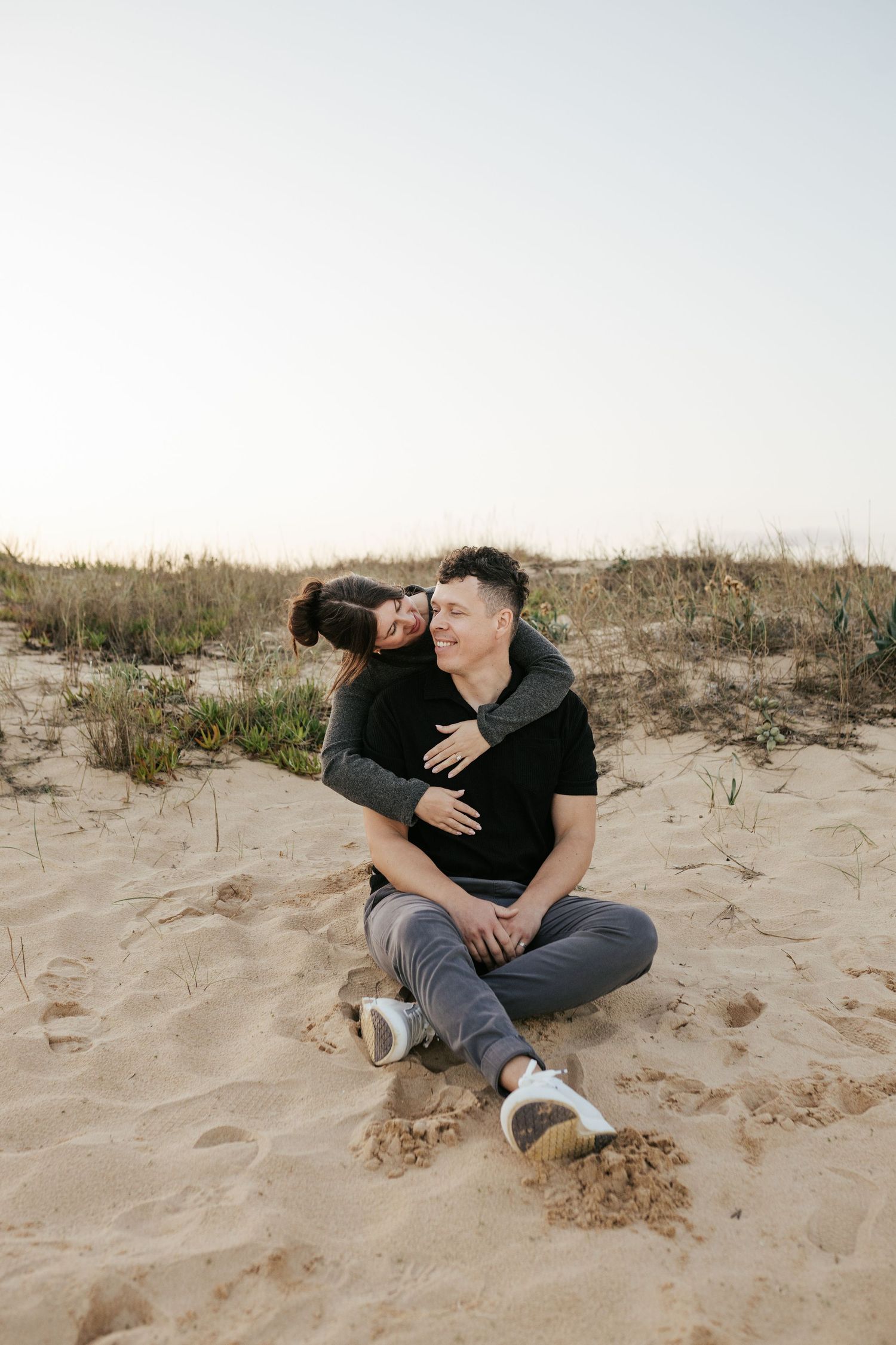 Couple sitting together on sand dunes during a casual beach photoshoot. Meia Praia, Lagos, Algarve, Portugal.