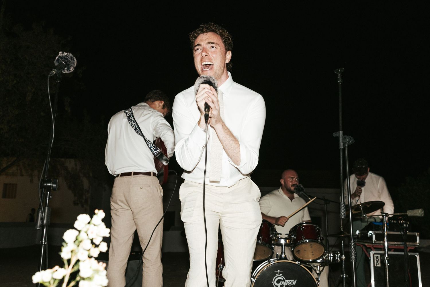 Male singer performing on stage with band at outdoor evening wedding reception.