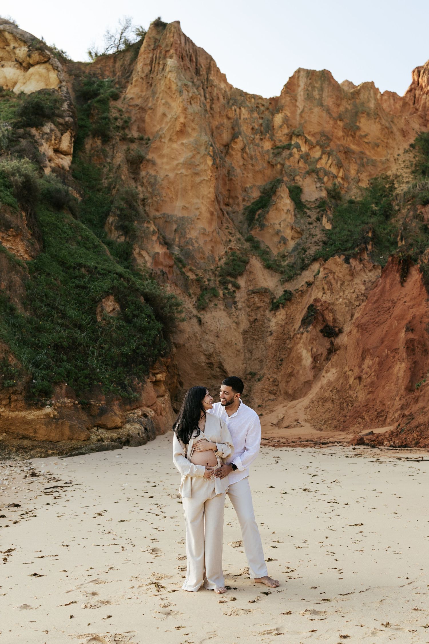 Couple embraces on secluded beach surrounded by towering orange cliffs. Praia do Camilo, Lagos, Algarve, Portugal.