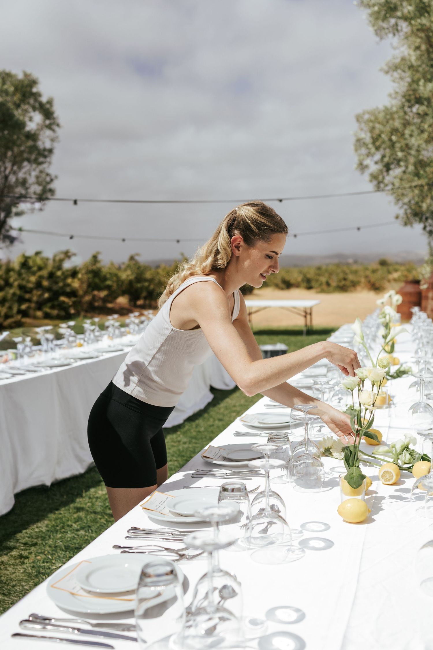 Woman setting an elegant outdoor dining table with lemon floral centerpieces for an event.