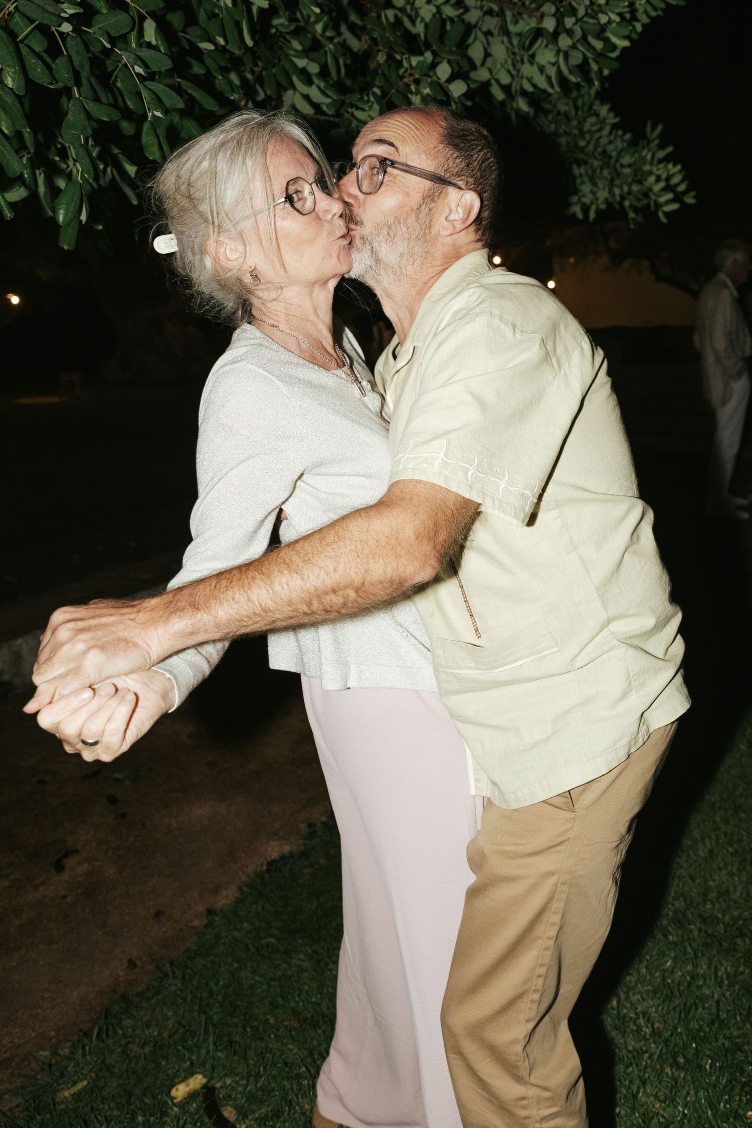 Older couple sharing a romantic kiss while dancing at an outdoor evening garden party.