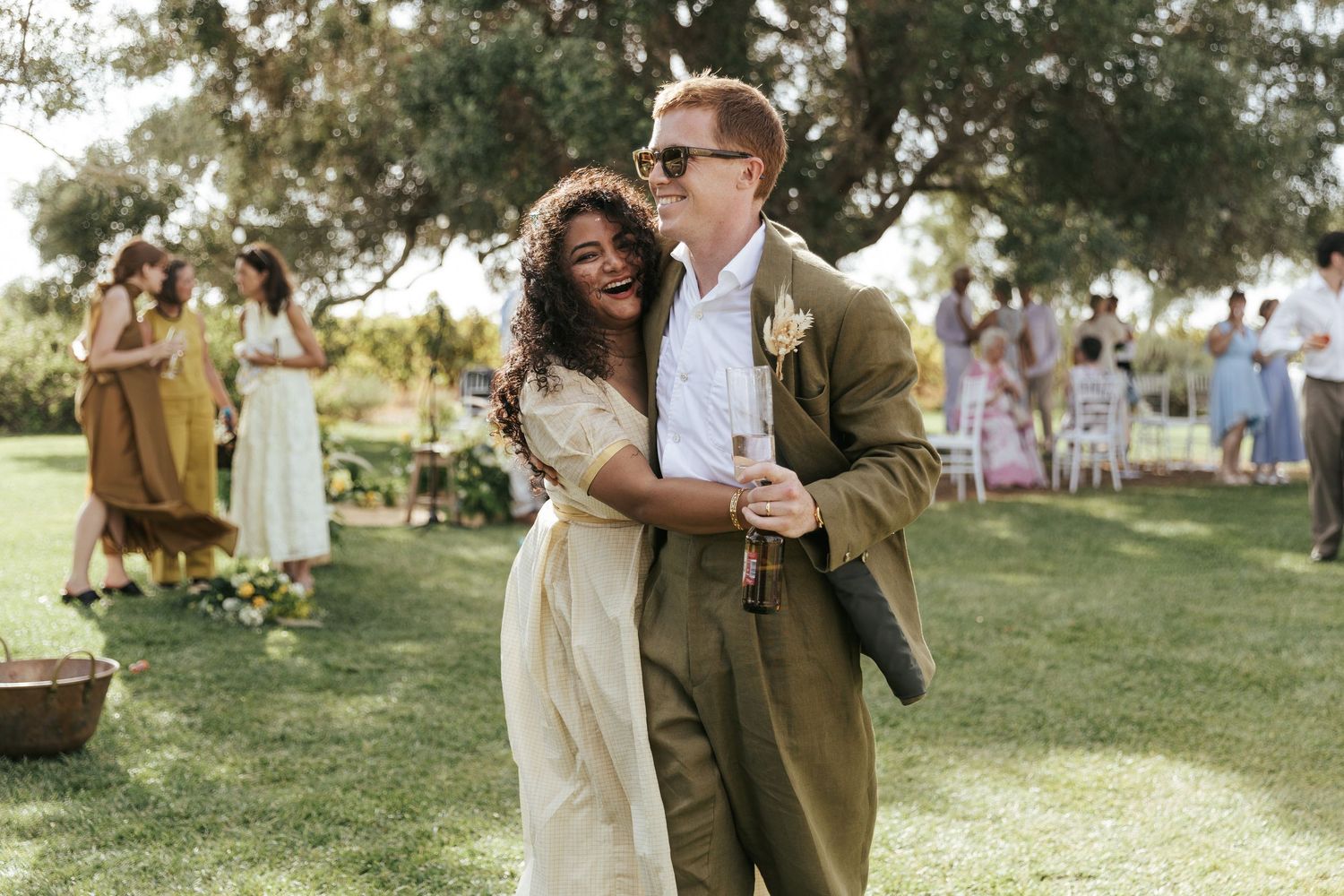 Happy couple embracing outdoors at a garden wedding reception, bride in ivory dress and groom in olive suit.