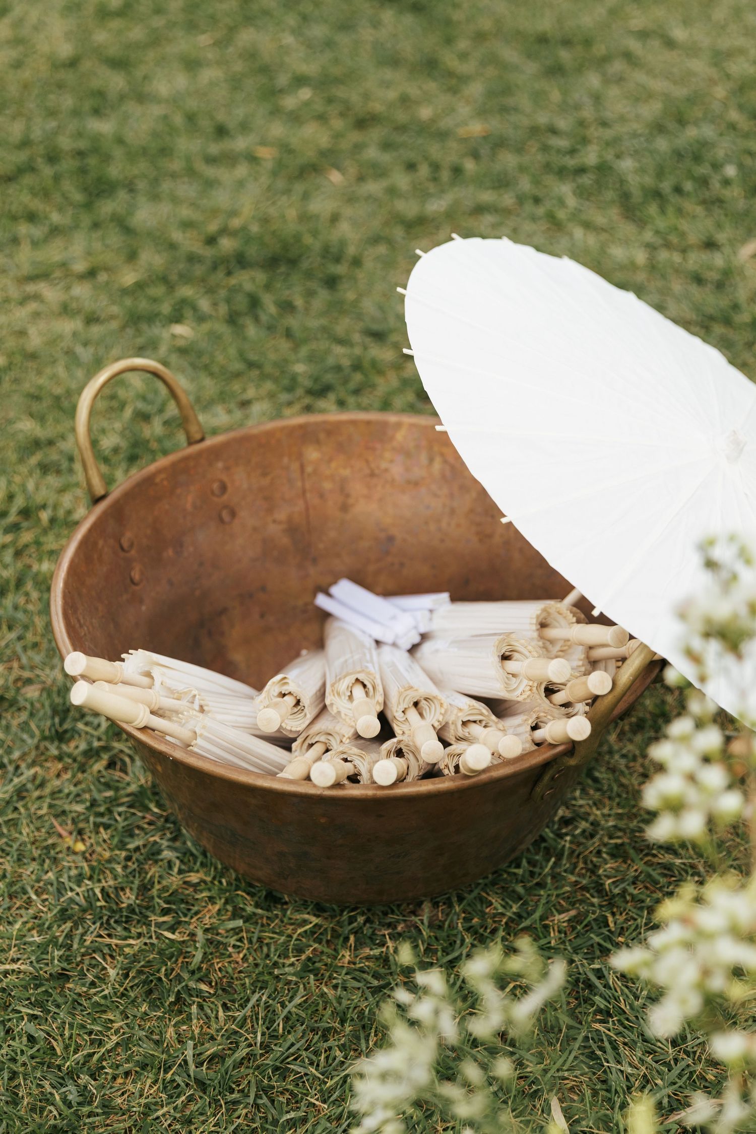 Rustic copper basin filled with wooden clothespins sits on green grass at an outdoor wedding or event.