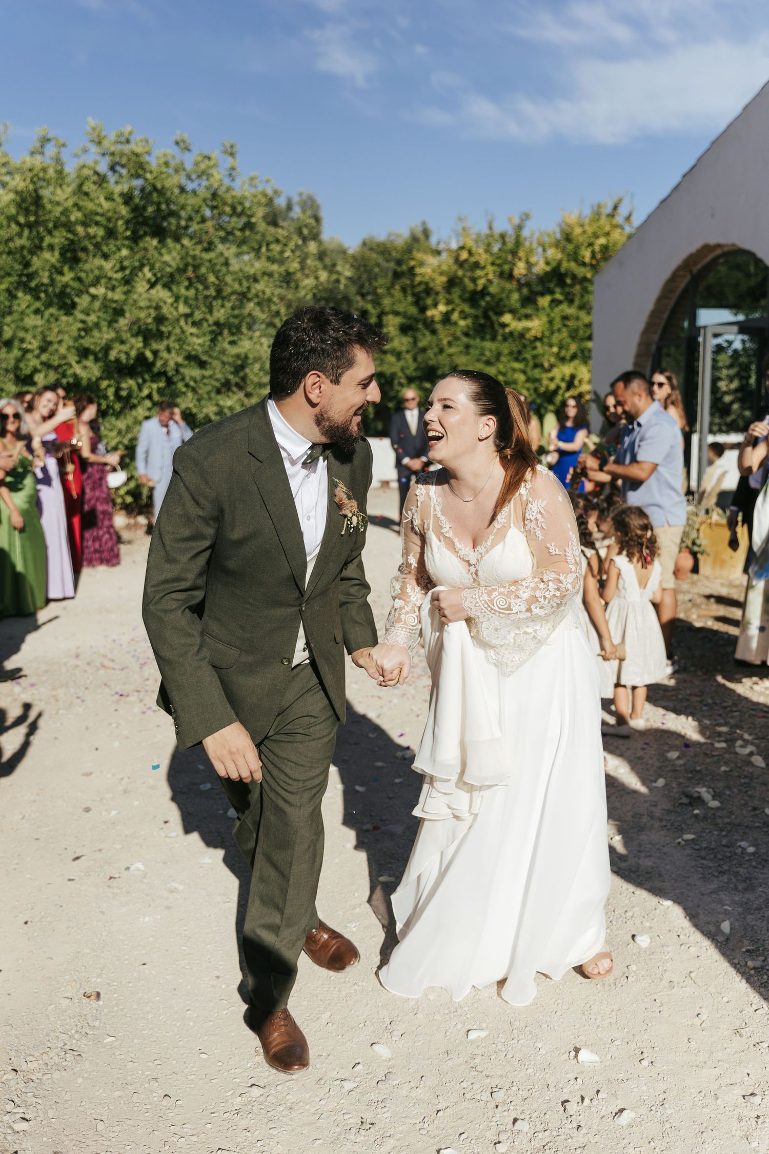 A couple shares joyful moments walking together on a sandy path at an outdoor wedding celebration.