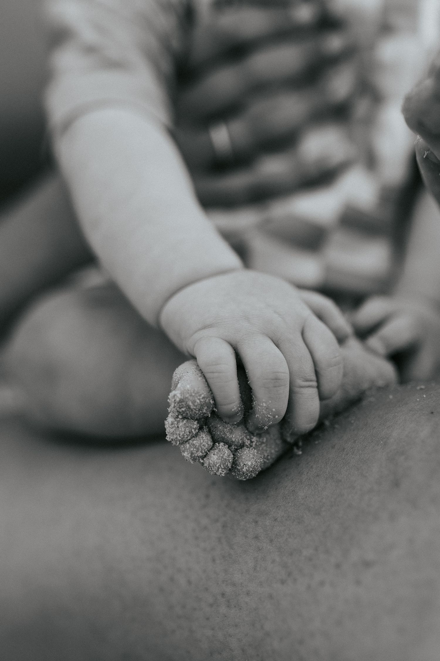 Close-up black and white image of a small child's hand playing with sand or dirt on a surface.