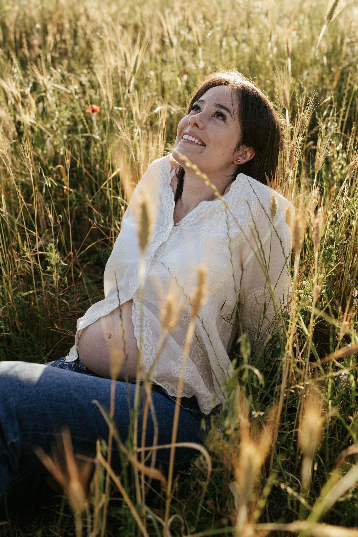 A person in a white shirt sits in a sunlit field of tall golden wheat during golden hour.
