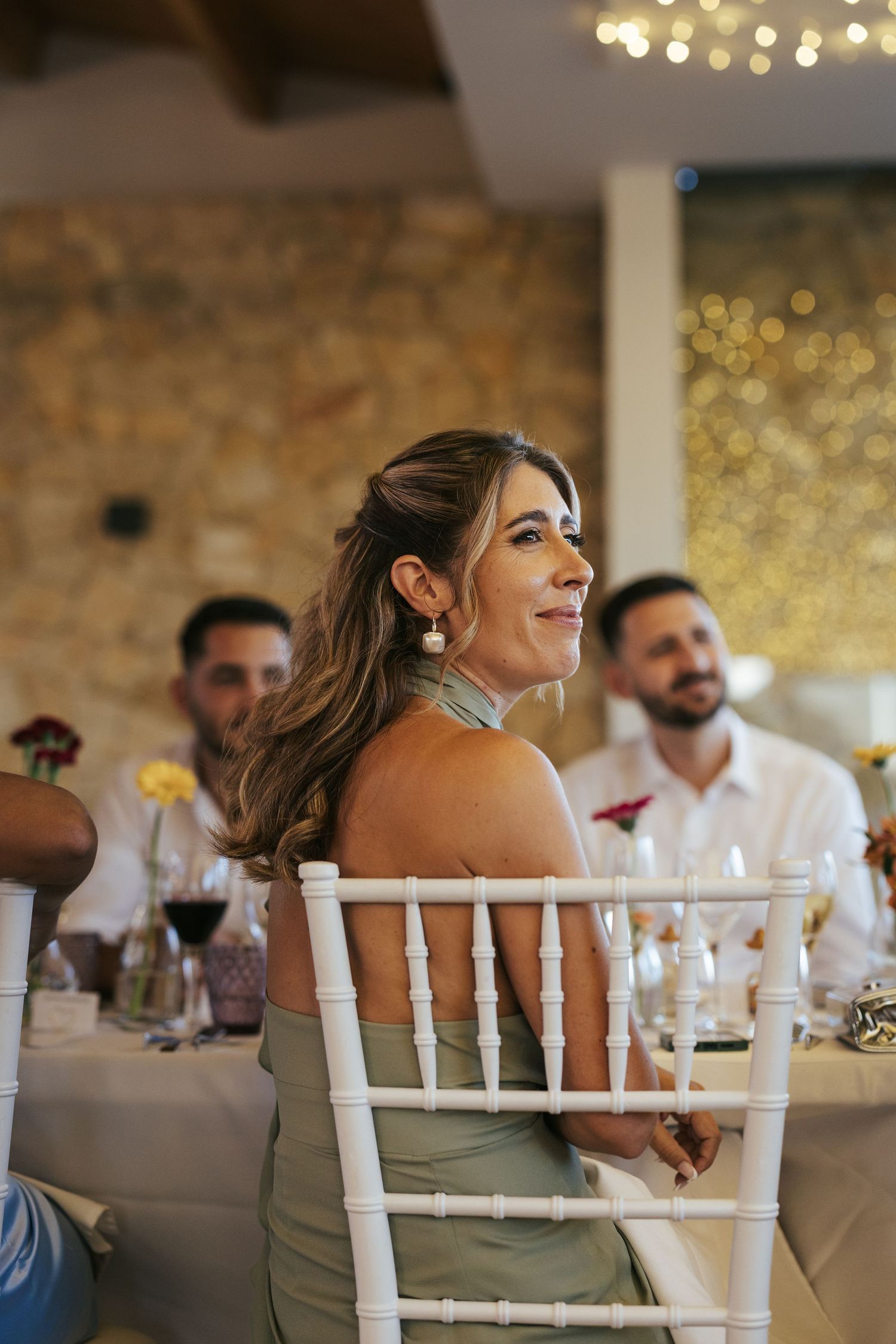 A guest at an indoor wedding reception sits in a white Chiavari chair, laughing joyfully during the celebration.