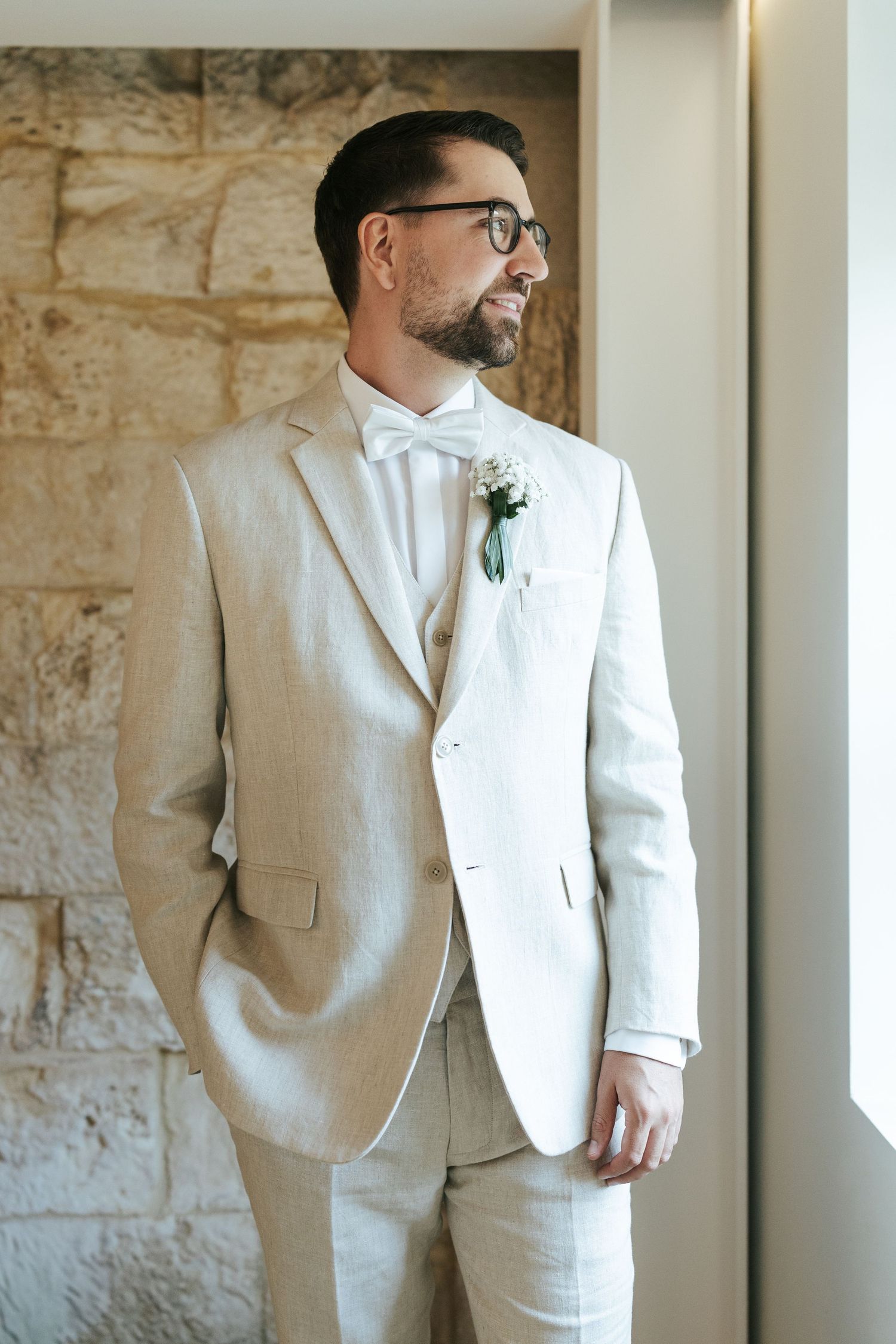 Elegant light colored suits displayed against a textured stone wall background.