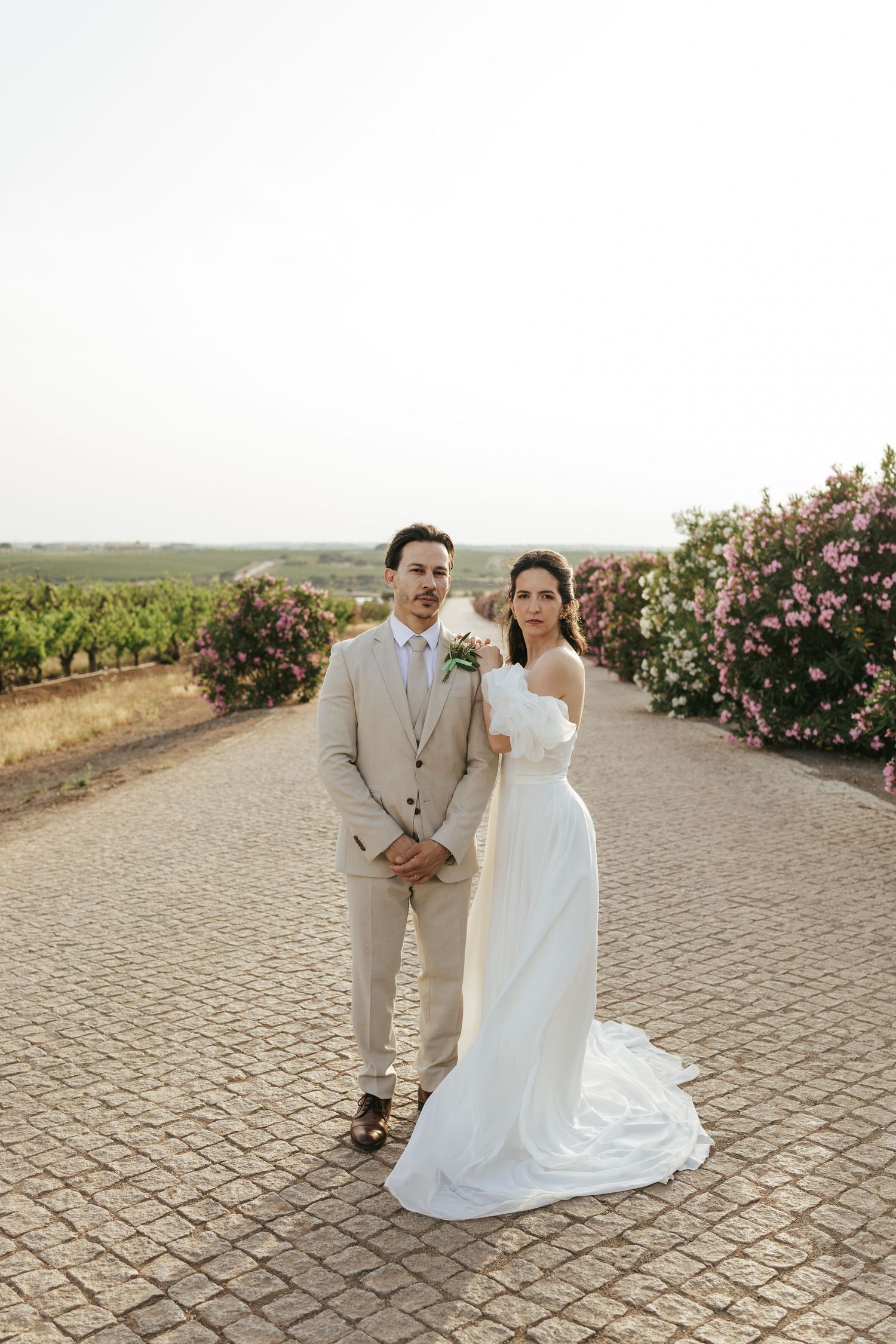 A couple shares a romantic moment on a cobblestone path surrounded by rose bushes and vineyard views.