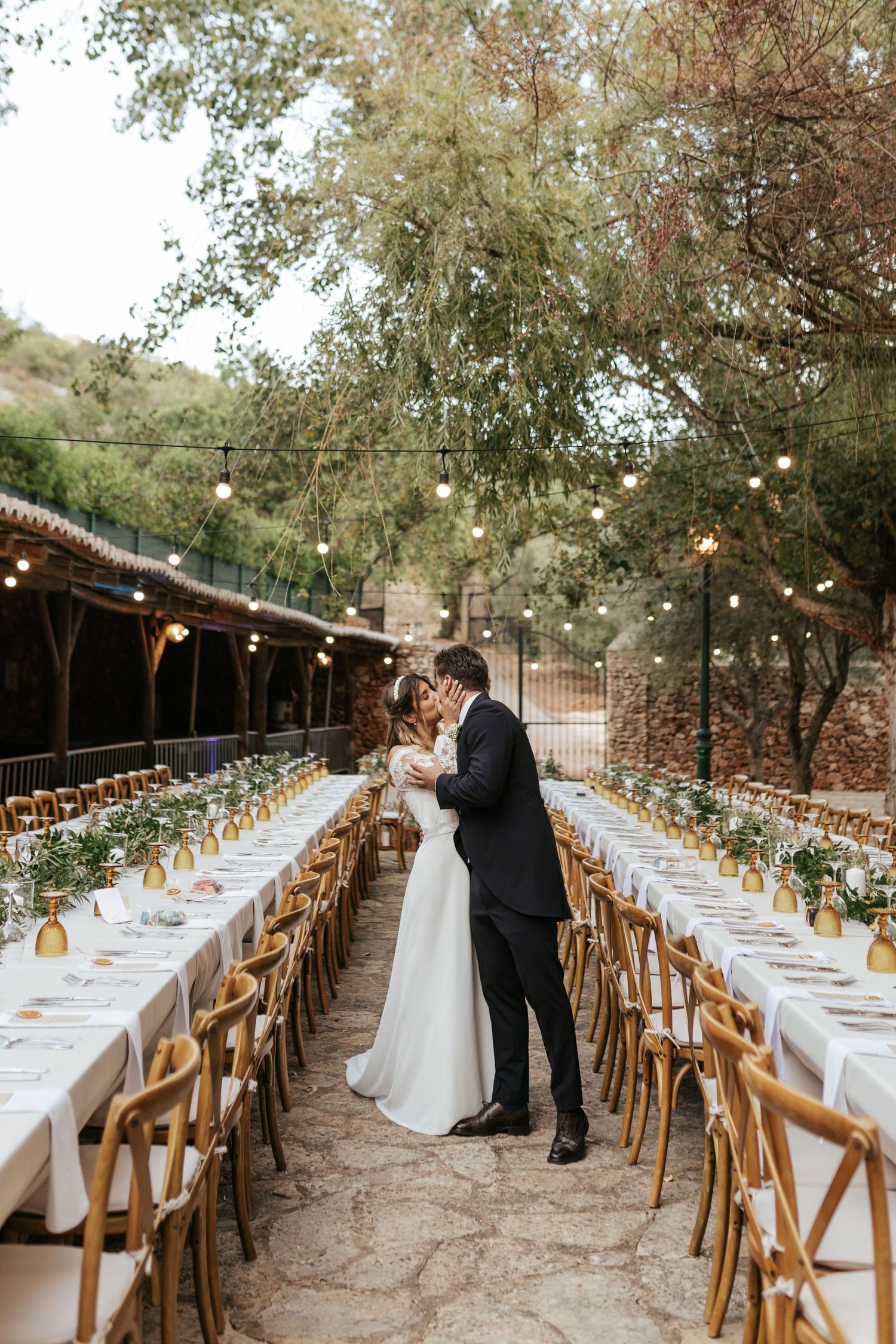 Enchanting outdoor wedding reception setup with long tables under string lights and rustic wooden chairs in a garden setting.