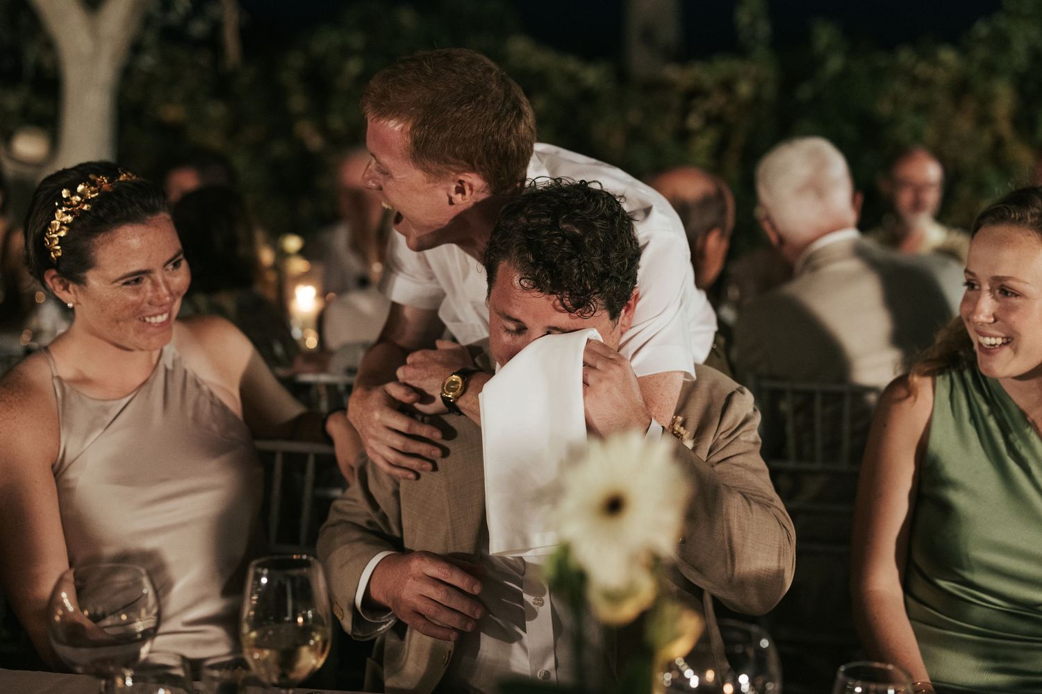 Joyful guests sharing a warm hug at an evening outdoor wedding reception.