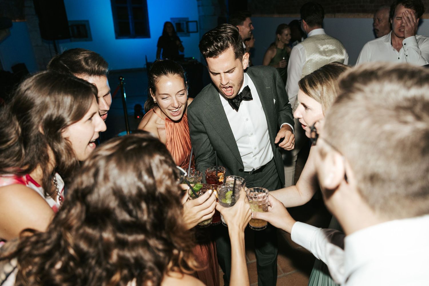 Wedding reception dance floor filled with guests celebrating under blue lighting.