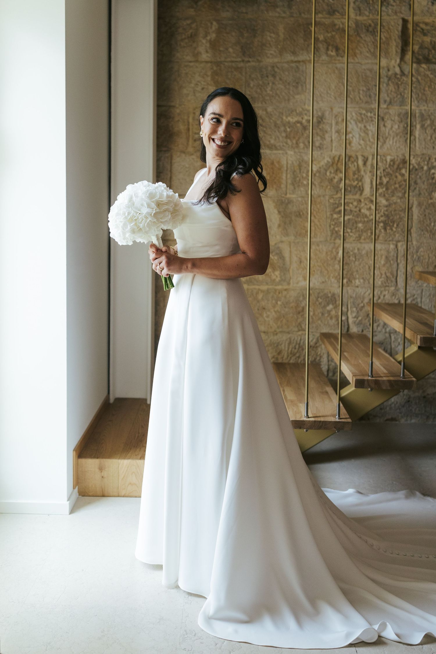 A flowing white wedding gown with a long train is showcased in an elegant indoor setting.