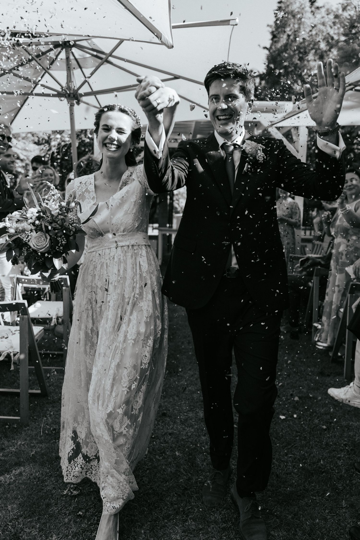 A vintage black and white wedding photo showing a couple celebrating under confetti with bunting in an outdoor garden setting.