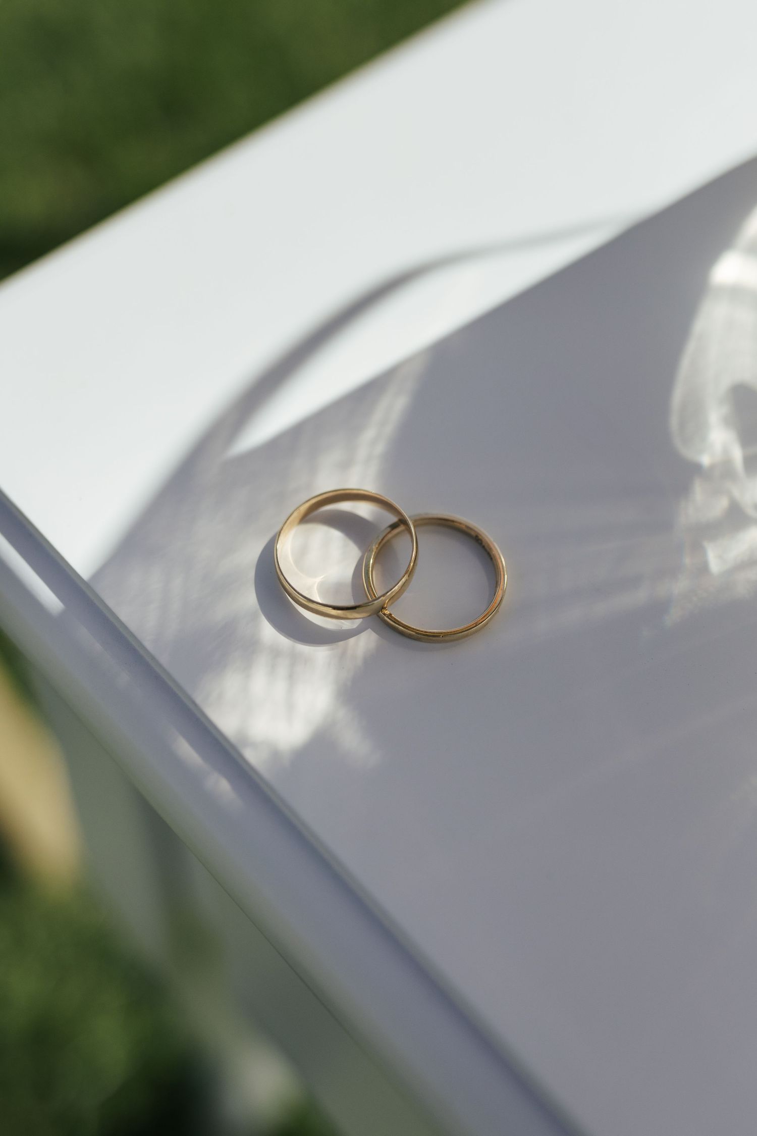 Two gold wedding rings rest on a white surface cast in natural light and shadows.