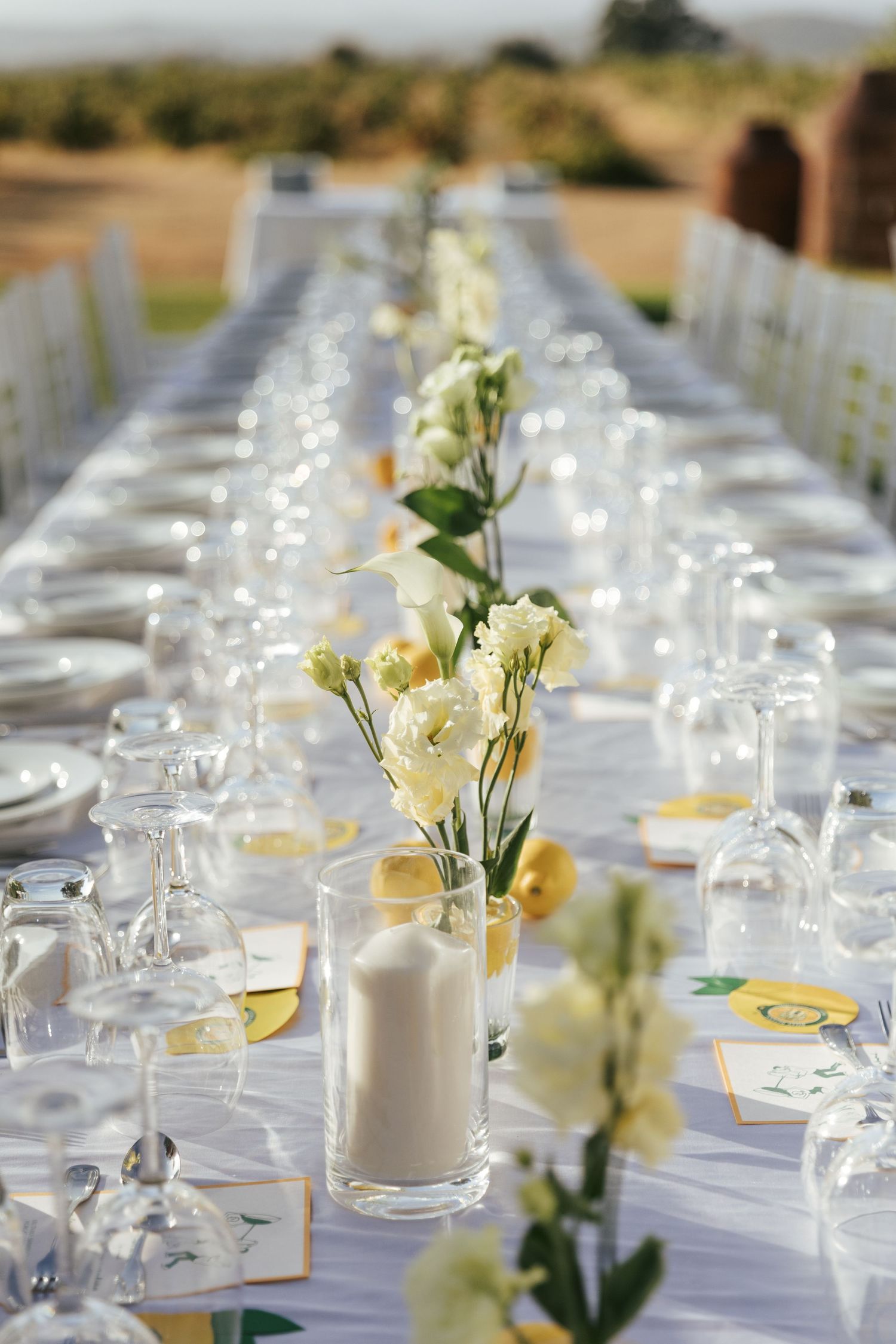 Elegant outdoor wedding reception table setting with white linens, candles, and delicate floral centerpieces.
