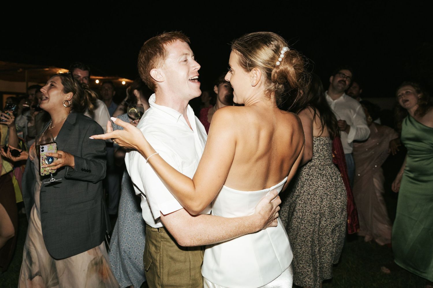 A couple dances together at a wedding reception while guests socialize in the background.