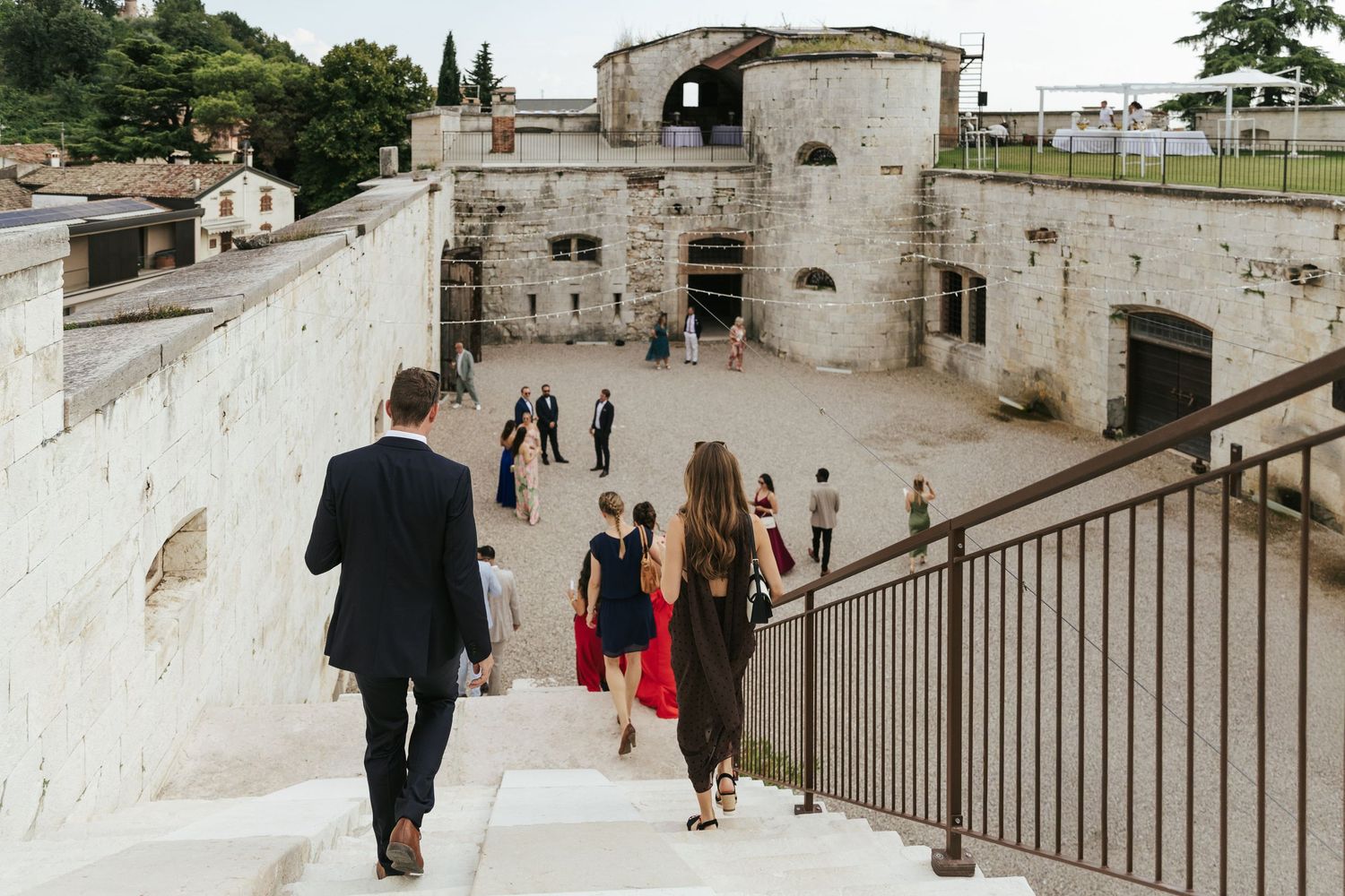 Stone architecture and stairs create a dramatic backdrop for wedding guests at a historic venue.