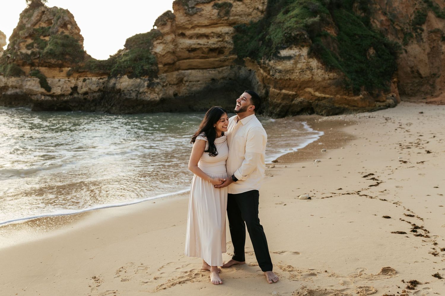 Couple embracing on a secluded beach cove with dramatic rocky cliffs. Praia do Camilo, Lagos, Algarve, Portugal.