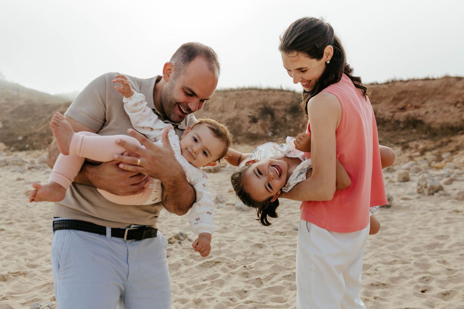 A family shares joyful moments together on a sandy beach with red rock formations in the background.